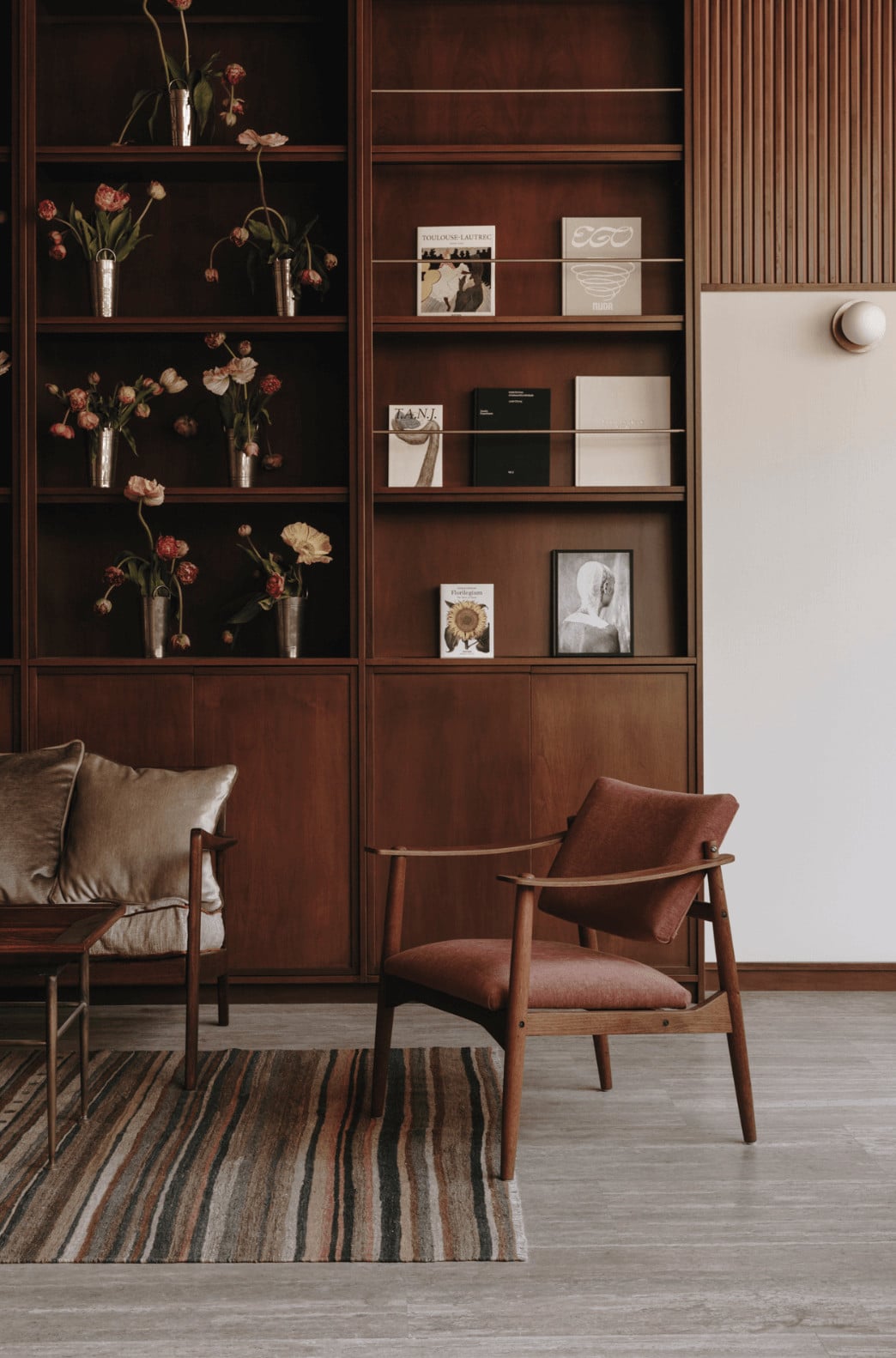 Parkhotel Mondschein, Europe — Walnut shelving with dried florals, mid-century lounge chairs, striped rug, and curated art in warm minimalist interior.