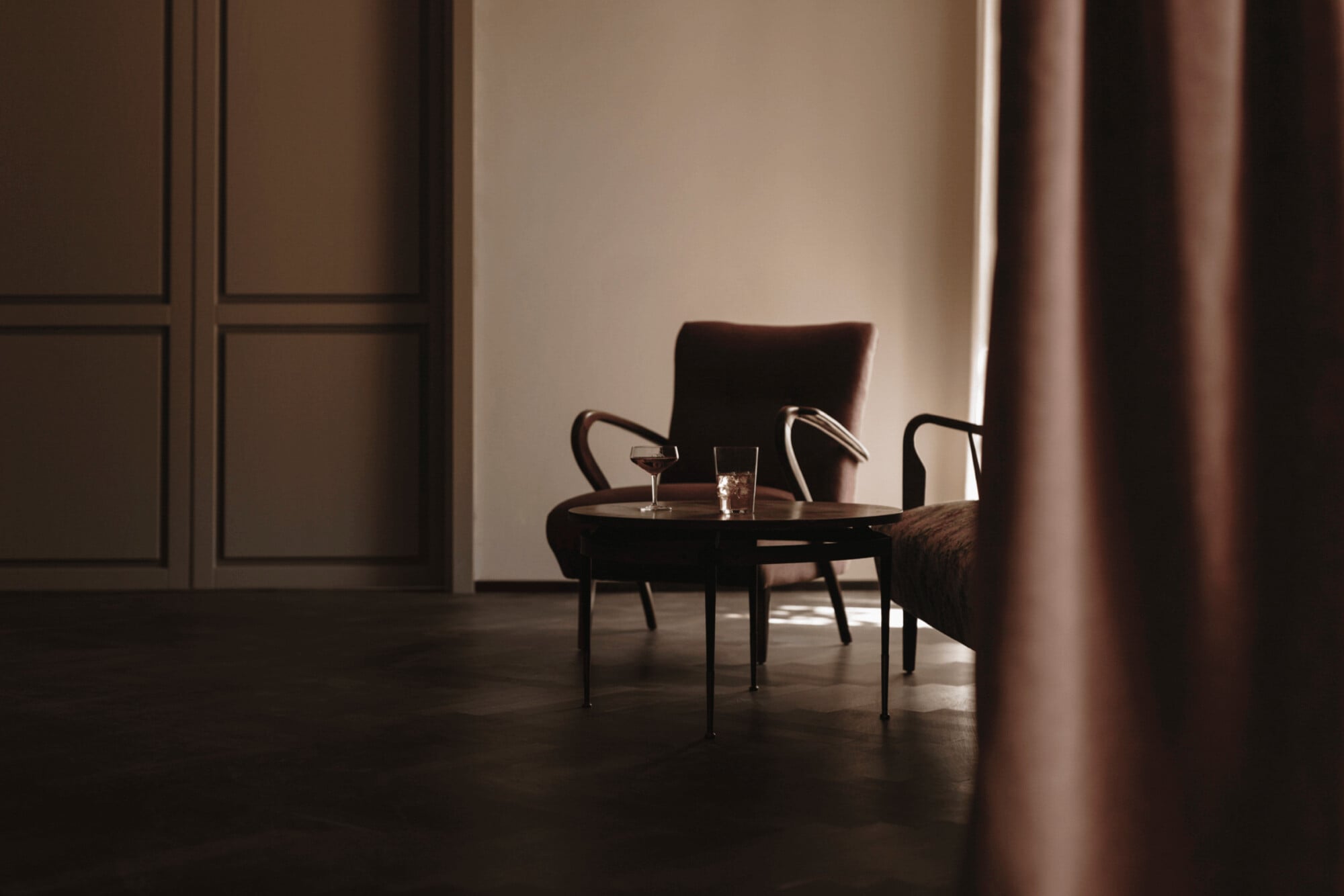 Parkhotel Mondschein, Europe — Minimalist lounge with mid-century modern chairs, round table, warm ambient lighting, and floor-to-ceiling curtains creating an elegant, serene interior space.