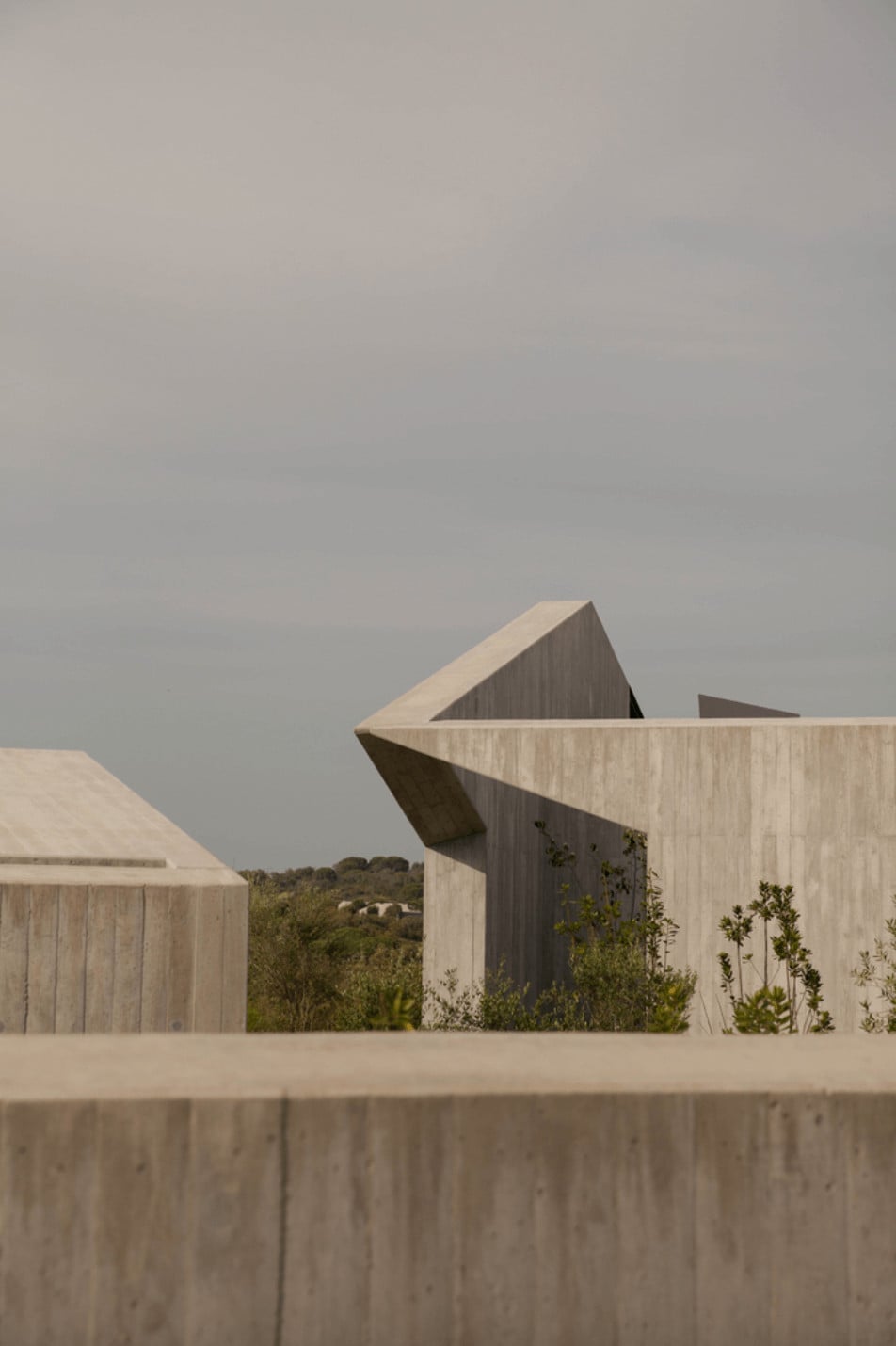 Pa.te.os, Europe — Geometric concrete architecture with angular wooden facades, minimalist design overlooking landscape, overcast sky, luxury hospitality aesthetic.