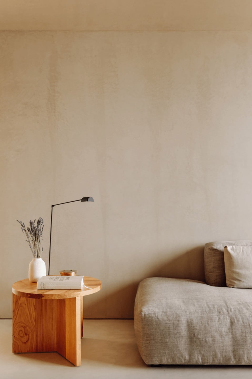 Pa.te.os, Europe — Minimalist living room with natural wood side table, linen upholstered sofa, dried flower arrangement, and sculptural floor lamp against neutral wall.