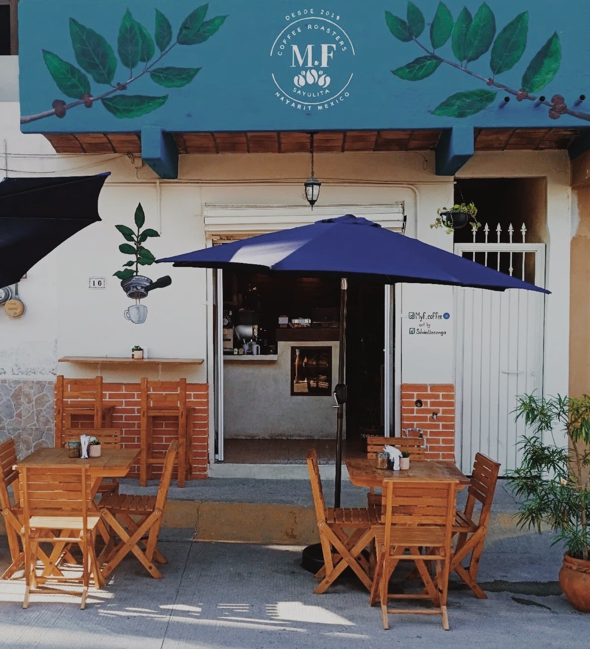 M&F Coffee Roasters storefront with blue awning, wooden chairs, and potted plants in colonial Mexican architecture.
