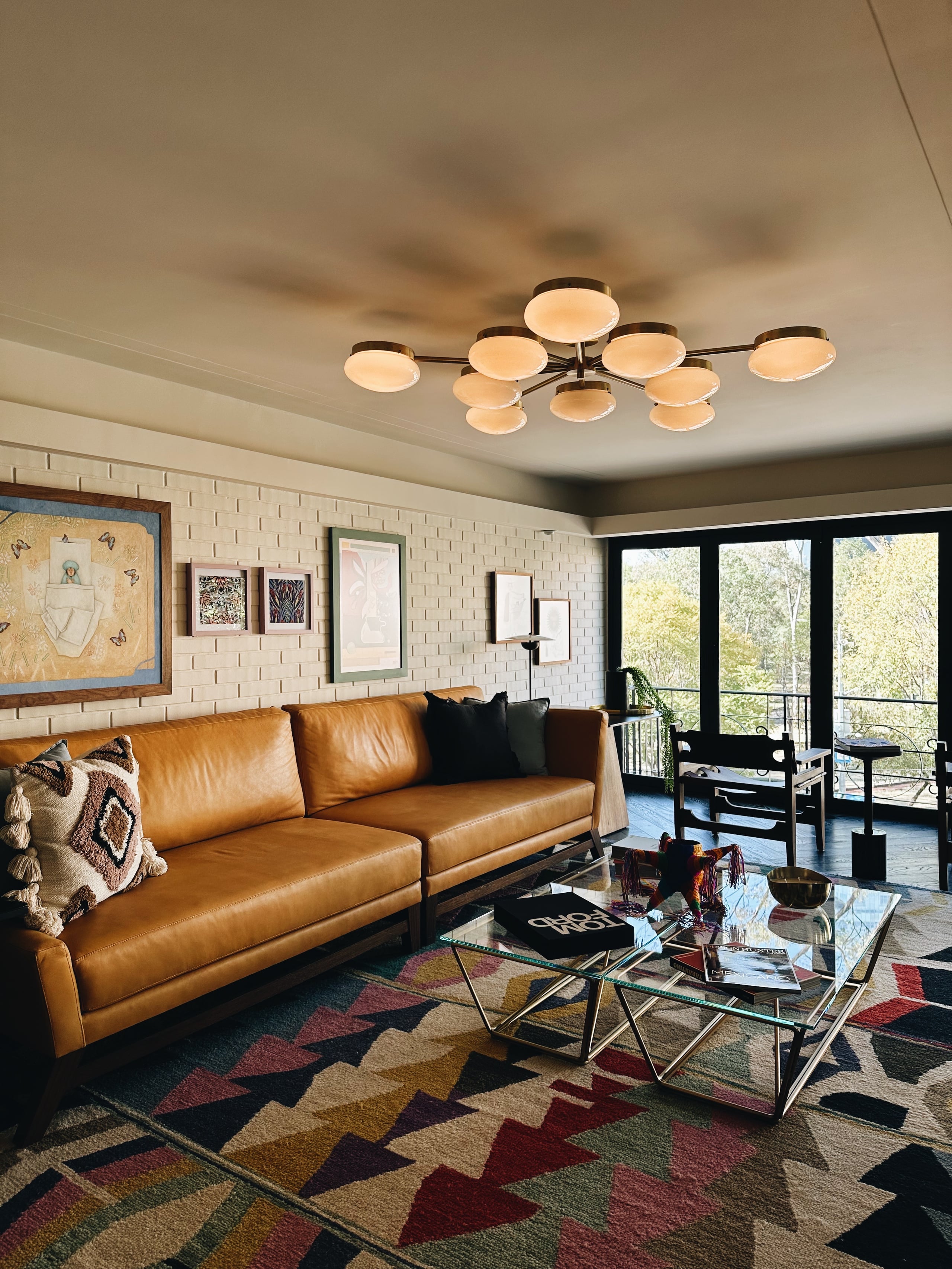 Campos Polanco, Mexico — Cognac leather sofa with geometric patterned rug, sculptural ceiling fixture, and floor-to-ceiling windows overlooking forest landscape in modern living room.