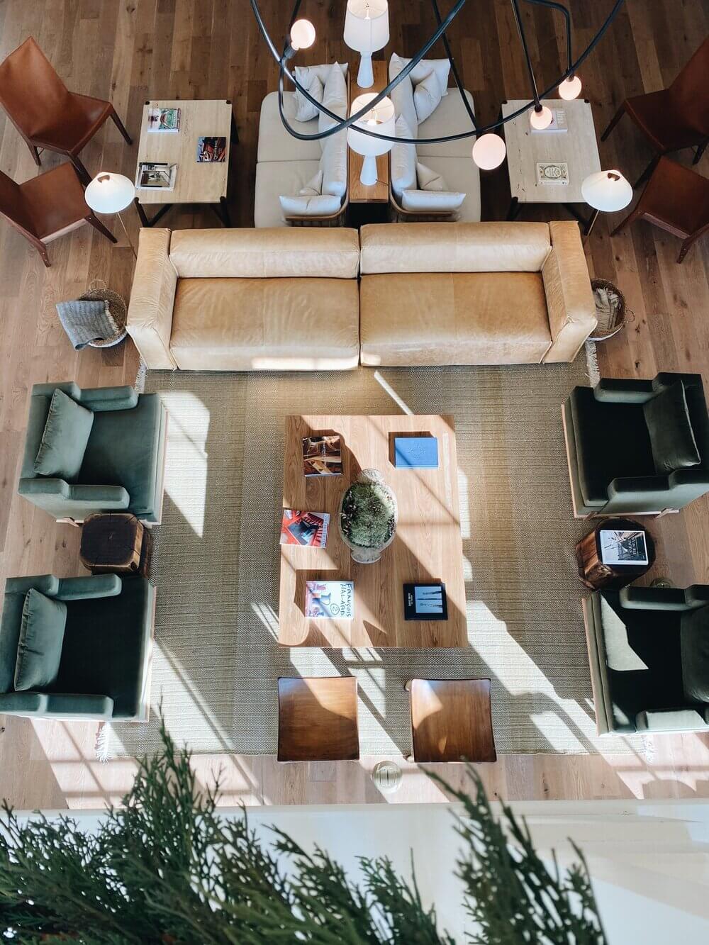 Overhead view of The Lake House lounge with cream seating, green chairs, warm wood flooring, and natural light streaming across a neutral rug.