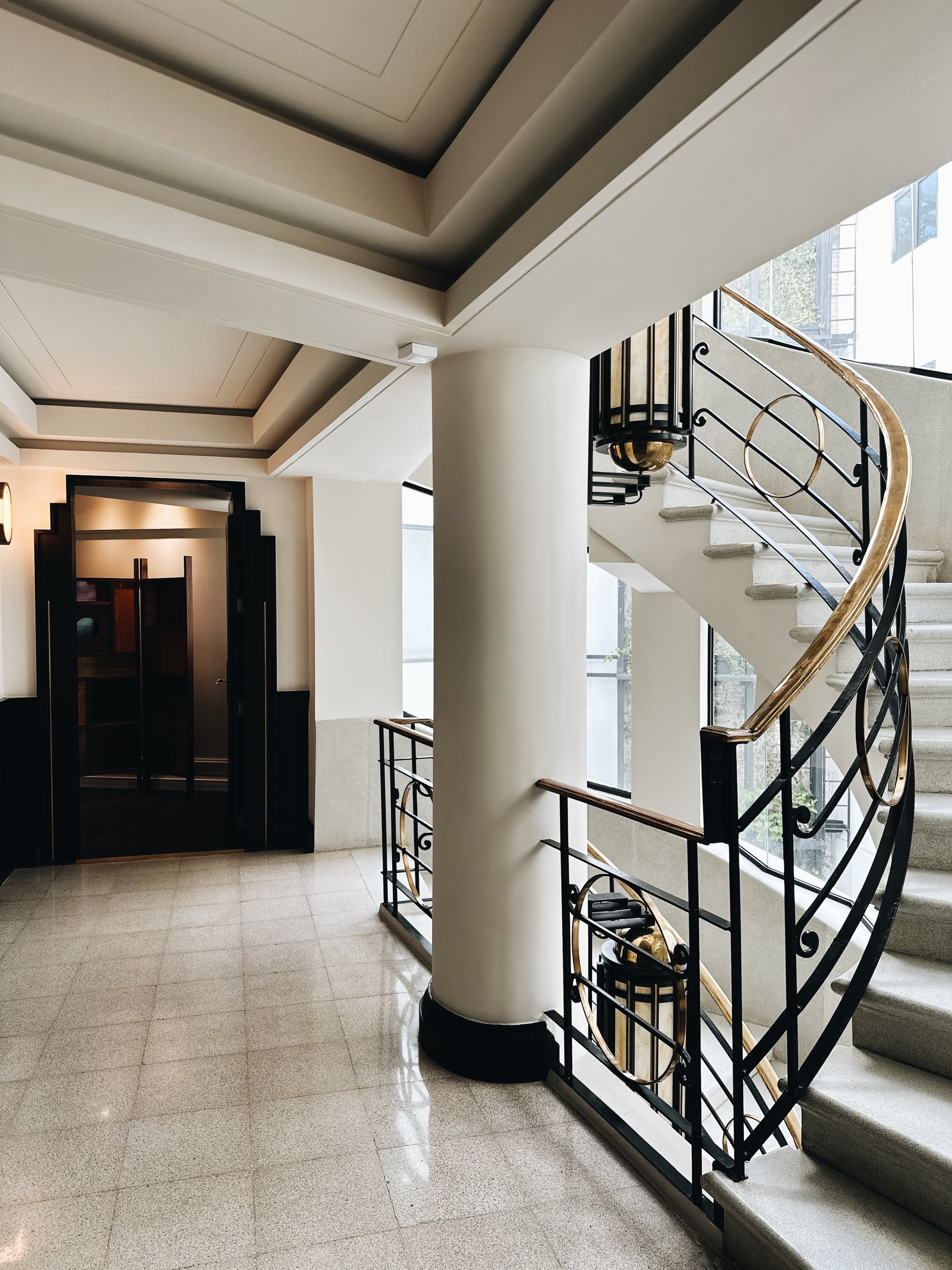 Campos Polanco, Mexico — Spiral staircase with black metal railings and wood handrail in minimalist concrete lobby with coffered ceiling and natural light.