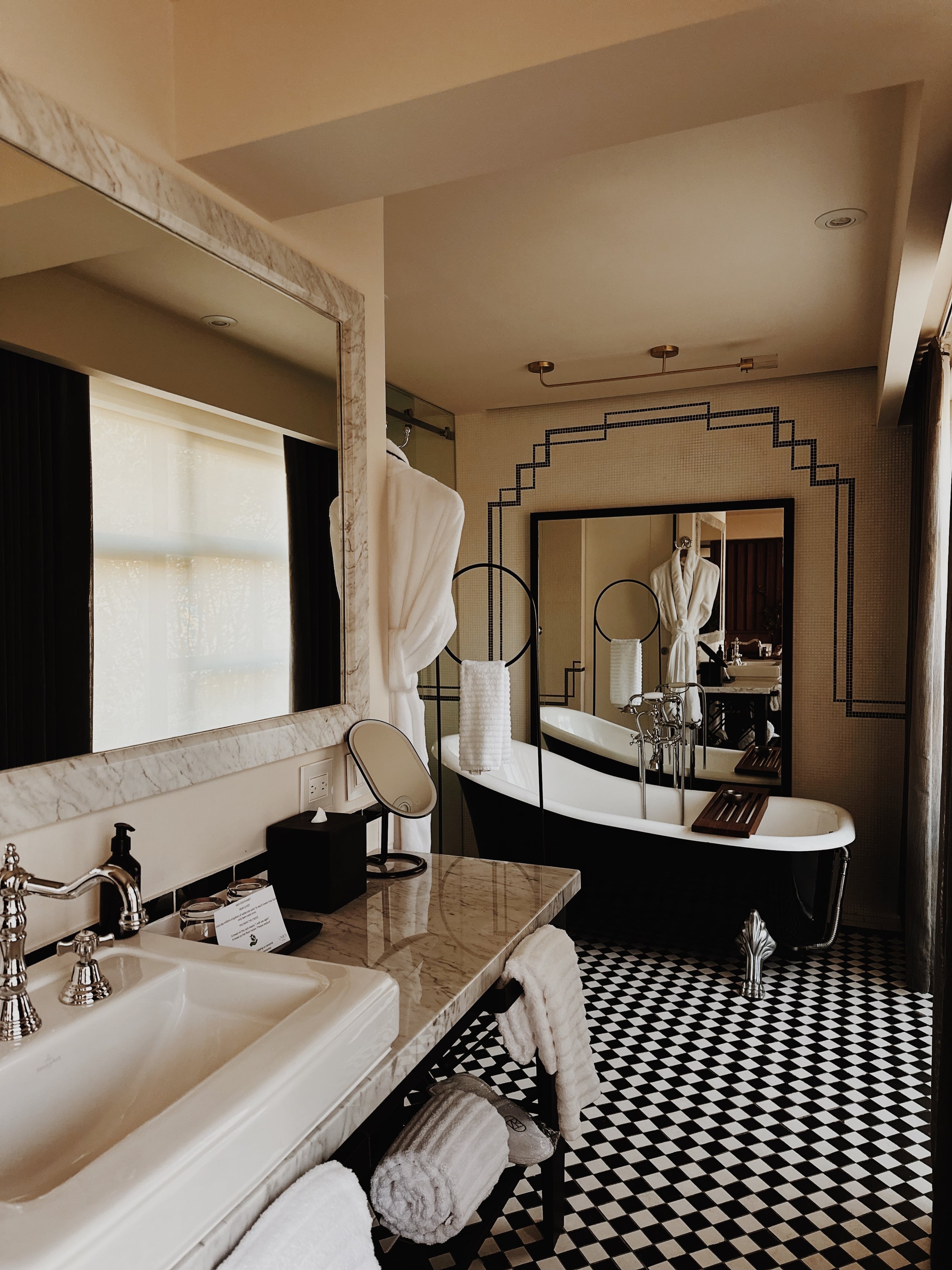 Campos Polanco, Mexico — Marble-accented bathroom with black freestanding tub, dual vanities, geometric mirror frame, and black-and-white checkered floor.