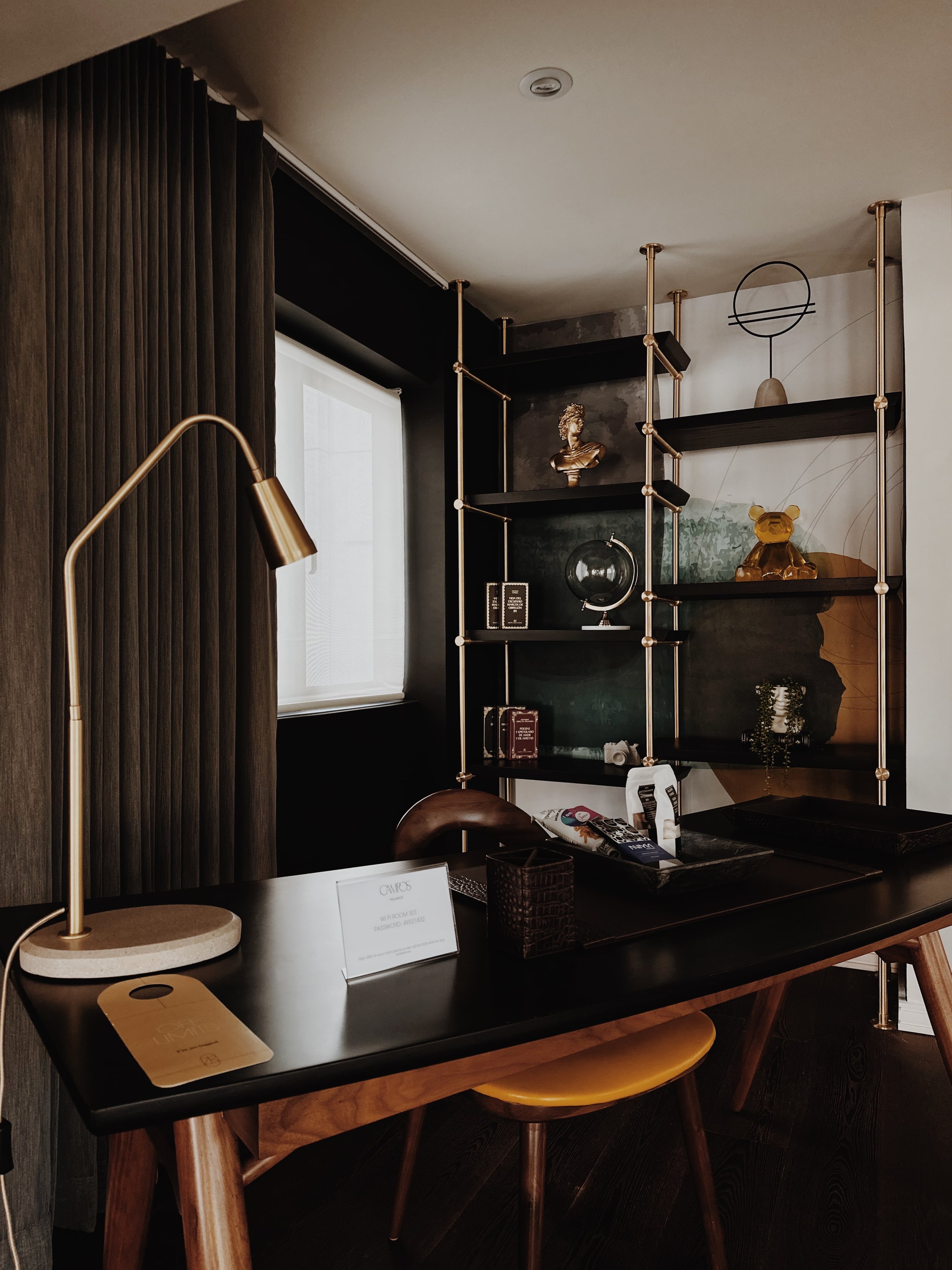 Campos Polanco, Mexico — Dark luxury office with brass arc lamp, black shelving, wooden mid-century chair, marble wall detail, and curated decorative objects.