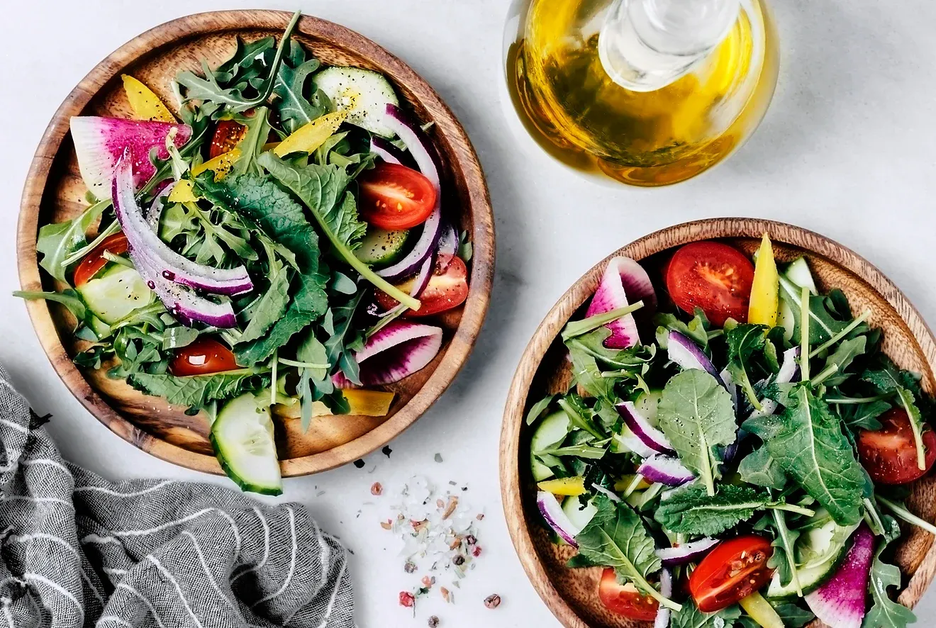 Piqniq, Balearic Islands — Two wooden bowls of vibrant salad with arugula, tomatoes, cucumber, and watermelon radish, olive oil, natural light.