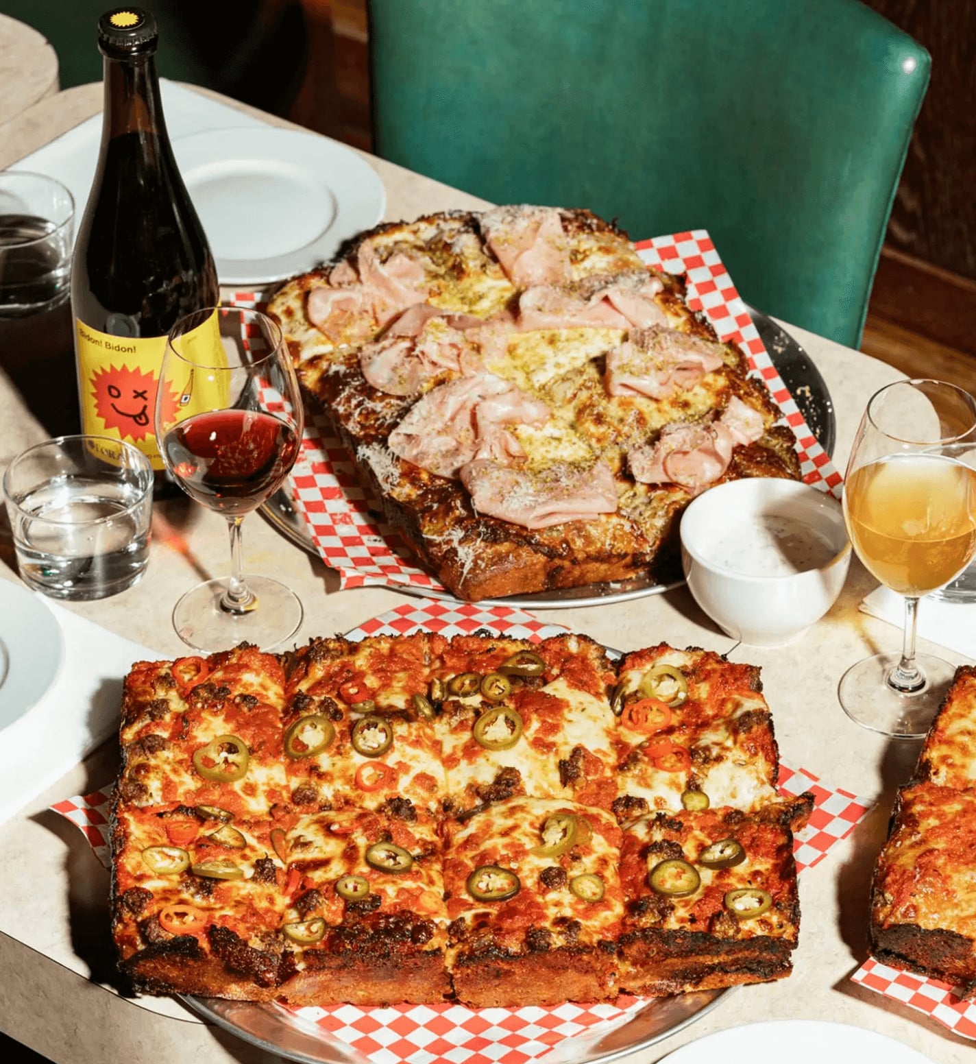 Four Corners, Europe — Detroit-style pizza with jalapeños and cured meats, wine service, green leather seating, natural light dining ambiance.
