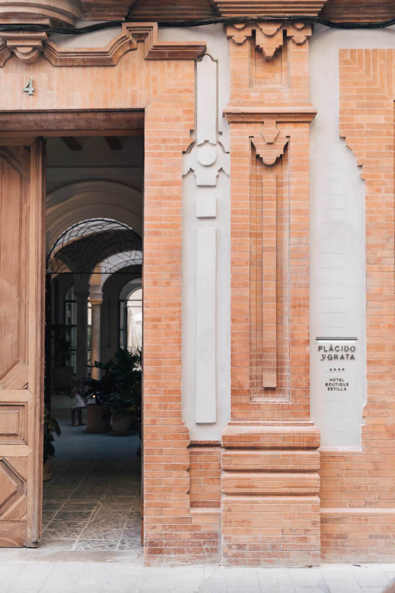 Plácido y Grata, Seville, Spain — Terracotta brick facade with white stone detailing, arched passageway, and carved corbels framing hotel entrance.