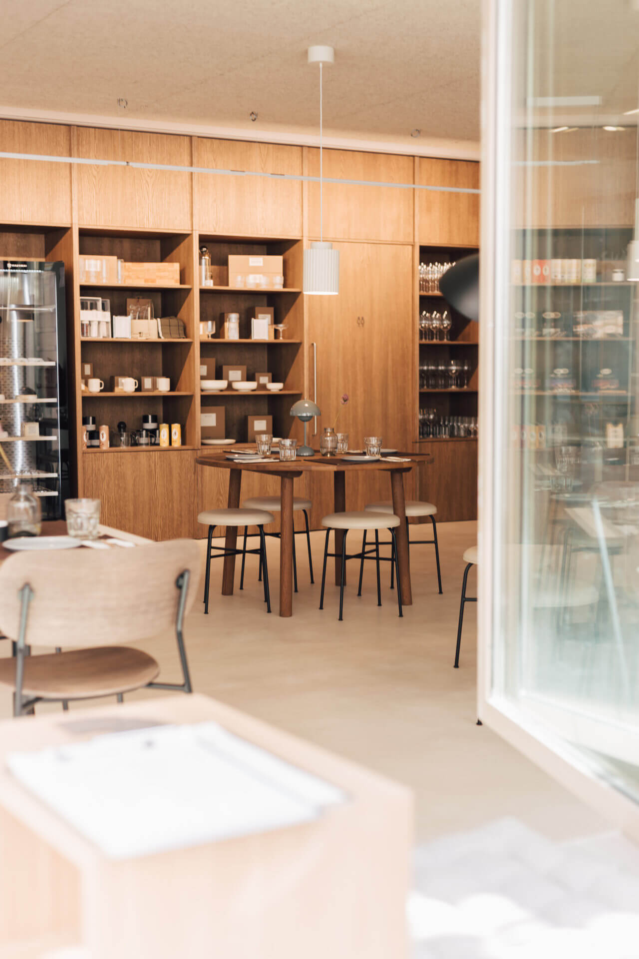 La Tienda, Europe — Minimalist retail interior with warm wood shelving, pendant lighting, and natural materials in a luxury hospitality design space.