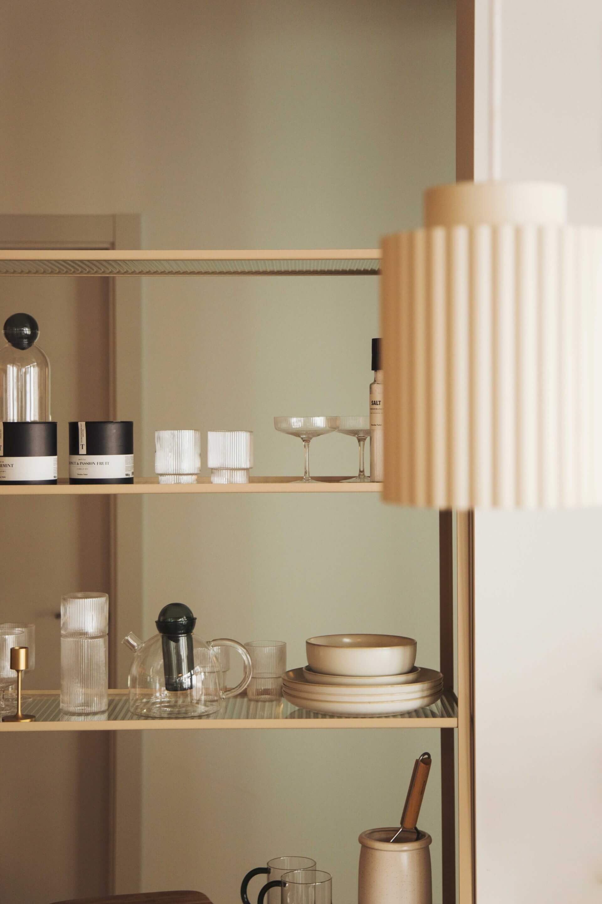 Plácido y Grata, Europe — Shelving with stacked ceramic tableware, glassware, and black accents beside pleated cream curtains in minimalist hospitality interior.