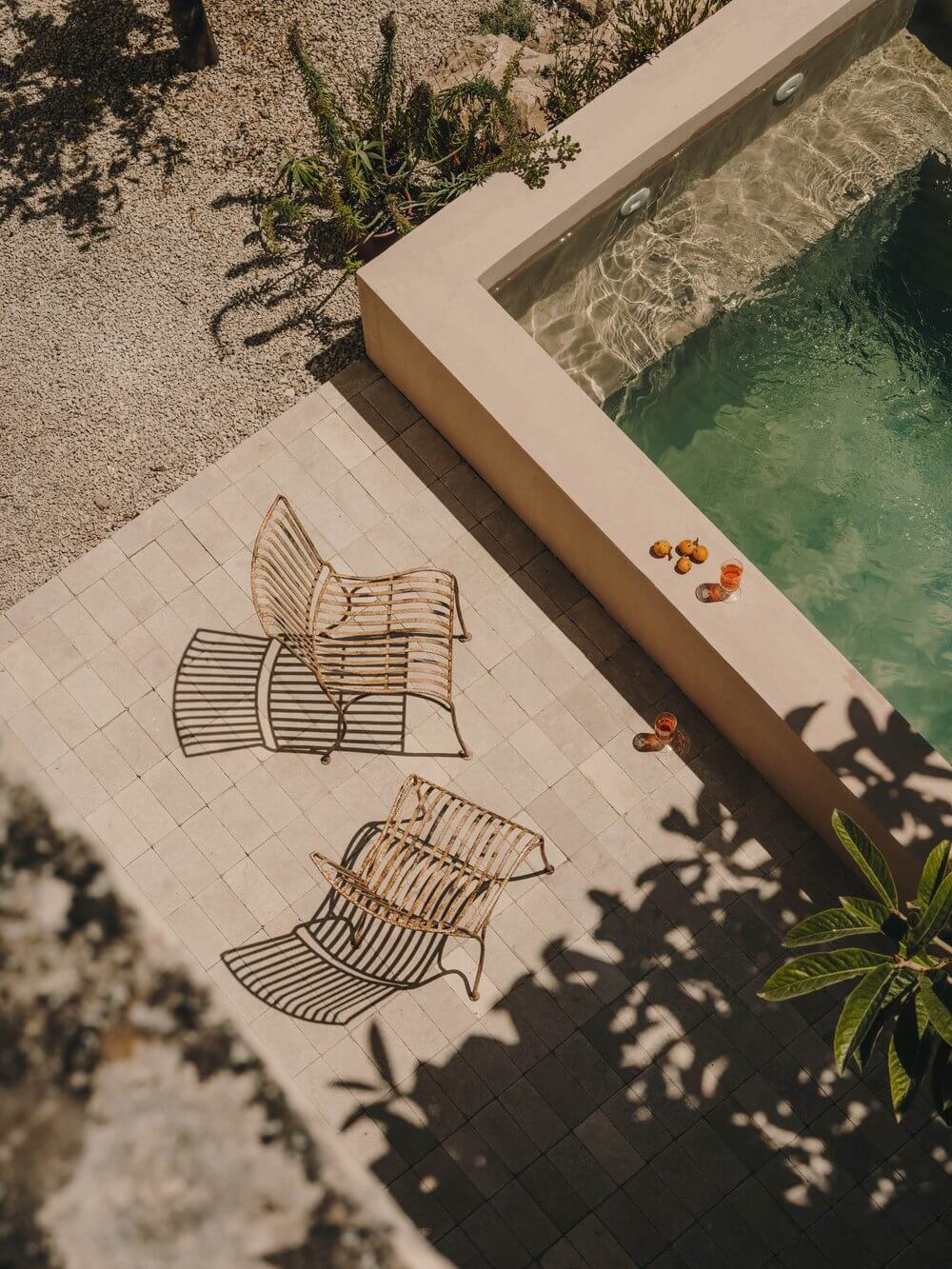 Casa Soleto, Europe — Poolside terrace with woven lounge chairs, green water, morning light casting shadows on pale tile deck.