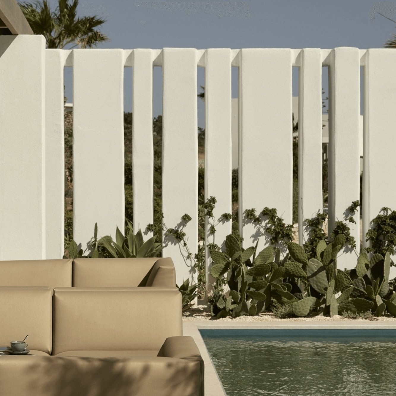 Pārocks, Europe — Minimalist poolside lounge with cream upholstered seating, white slatted privacy screen, and desert plantings overlooking still water.