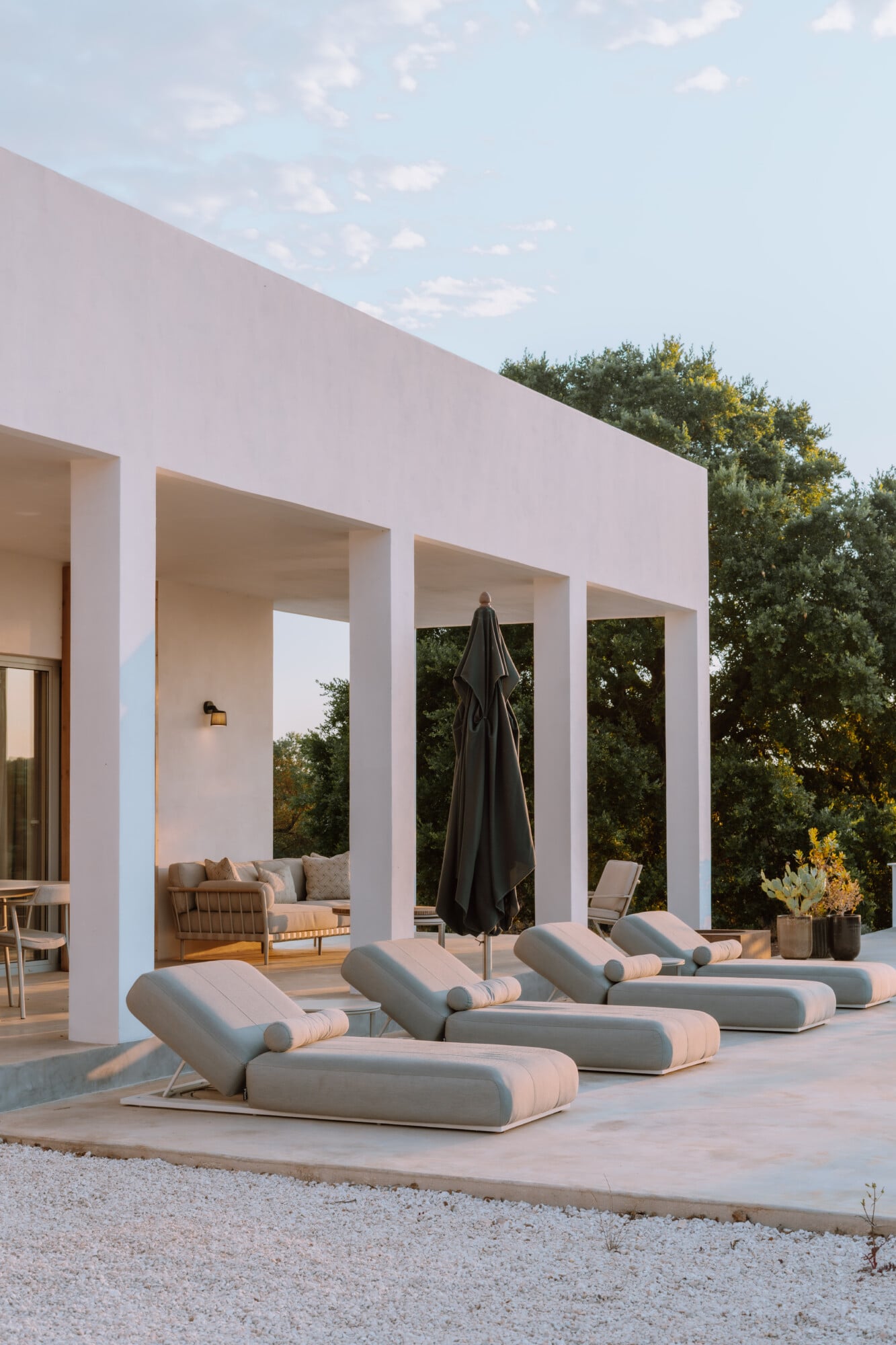 Villa Quercia, Italy — Modernist poolside loggia with sculptural loungers, black umbrella, and olive trees under Mediterranean light.