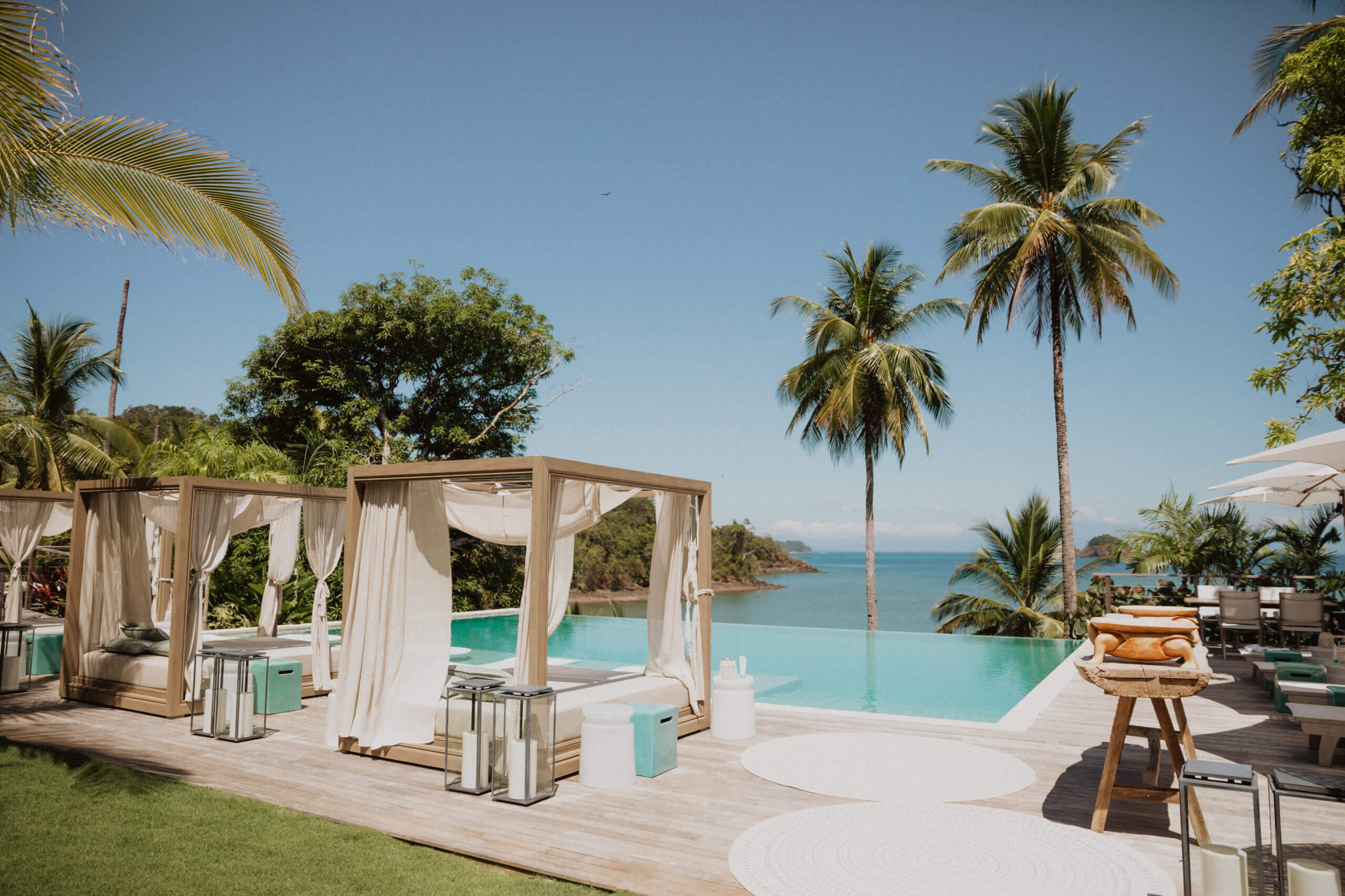 Islas Secas — Infinity pool with draped cabanas overlooking turquoise bay, palm trees, teak deck, tropical coastal luxury resort.