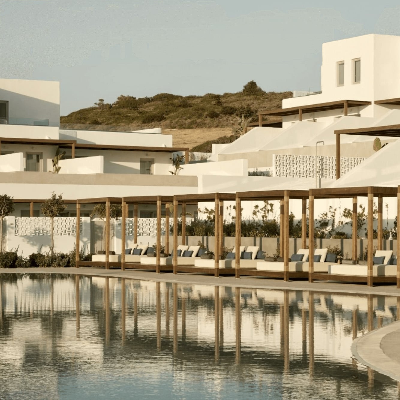 Pārocks, Europe — Minimalist white pavilions with timber pergolas overlooking still reflecting pool, terraced hillside setting, contemporary luxury resort architecture.