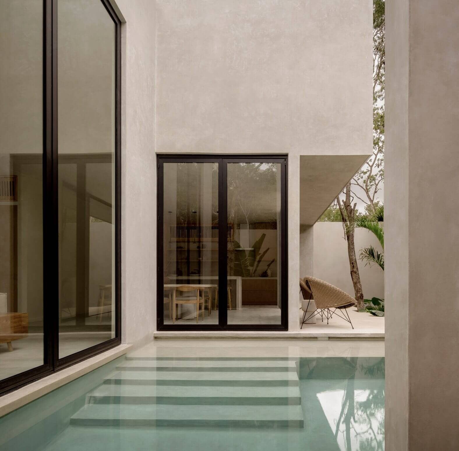 Villa Cava, Mexico — Minimalist courtyard with glass doors, pale stucco walls, reflecting pool, and climbing vines creating serene modernist architecture.