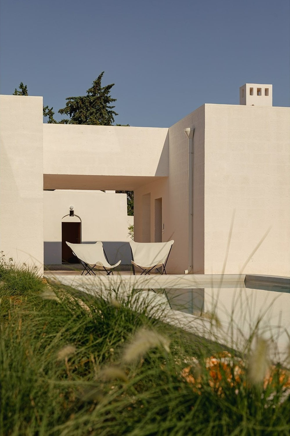 Casanguilla, Europe — Minimalist cream-stone villa with geometric volumes, angular canopy, and infinity pool reflecting modernist architecture against clear sky.