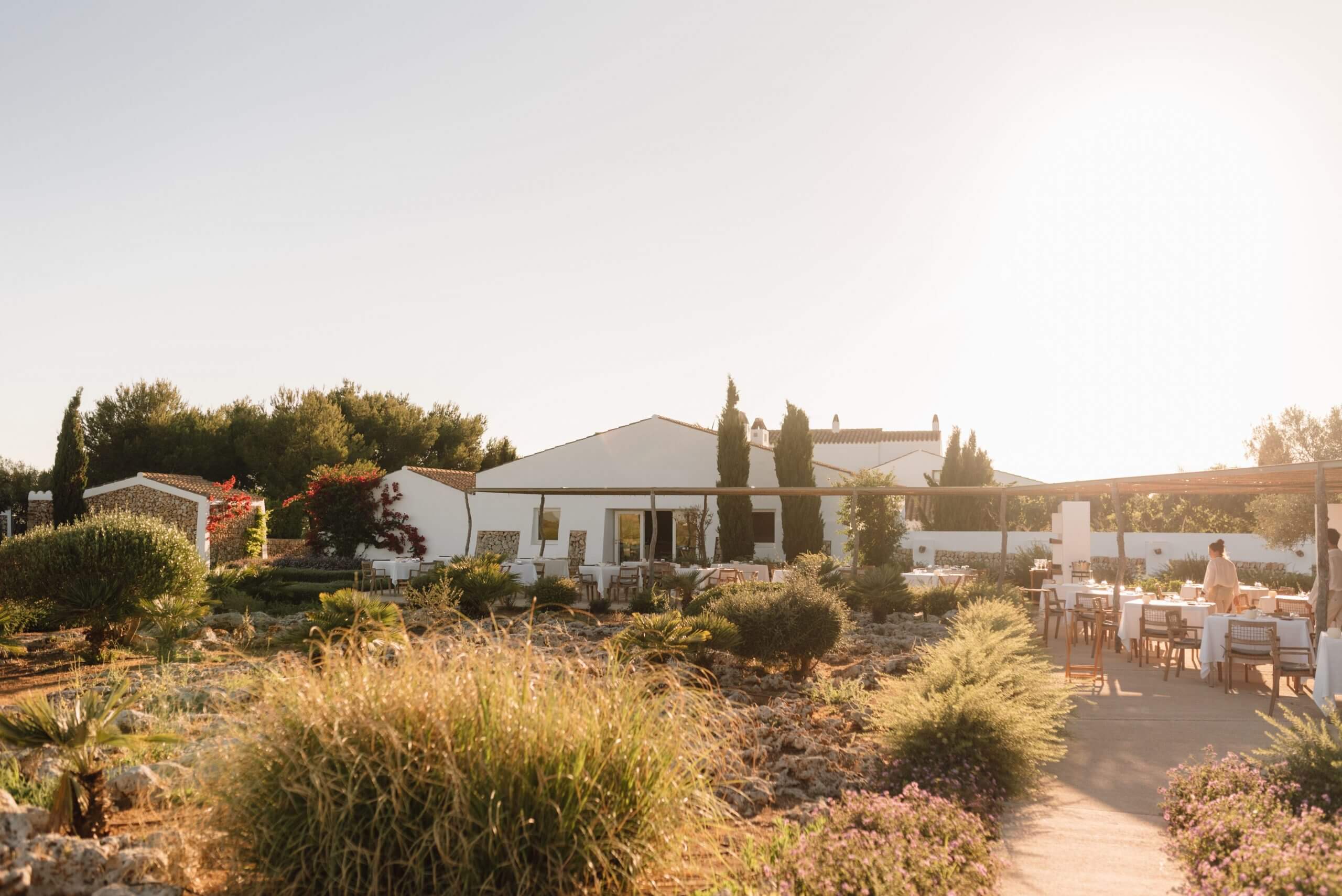 Torralbenc, Balearic Islands — Whitewashed Mediterranean villa with cypress trees, terracotta dining terrace, and drought-resistant landscaping at golden hour.