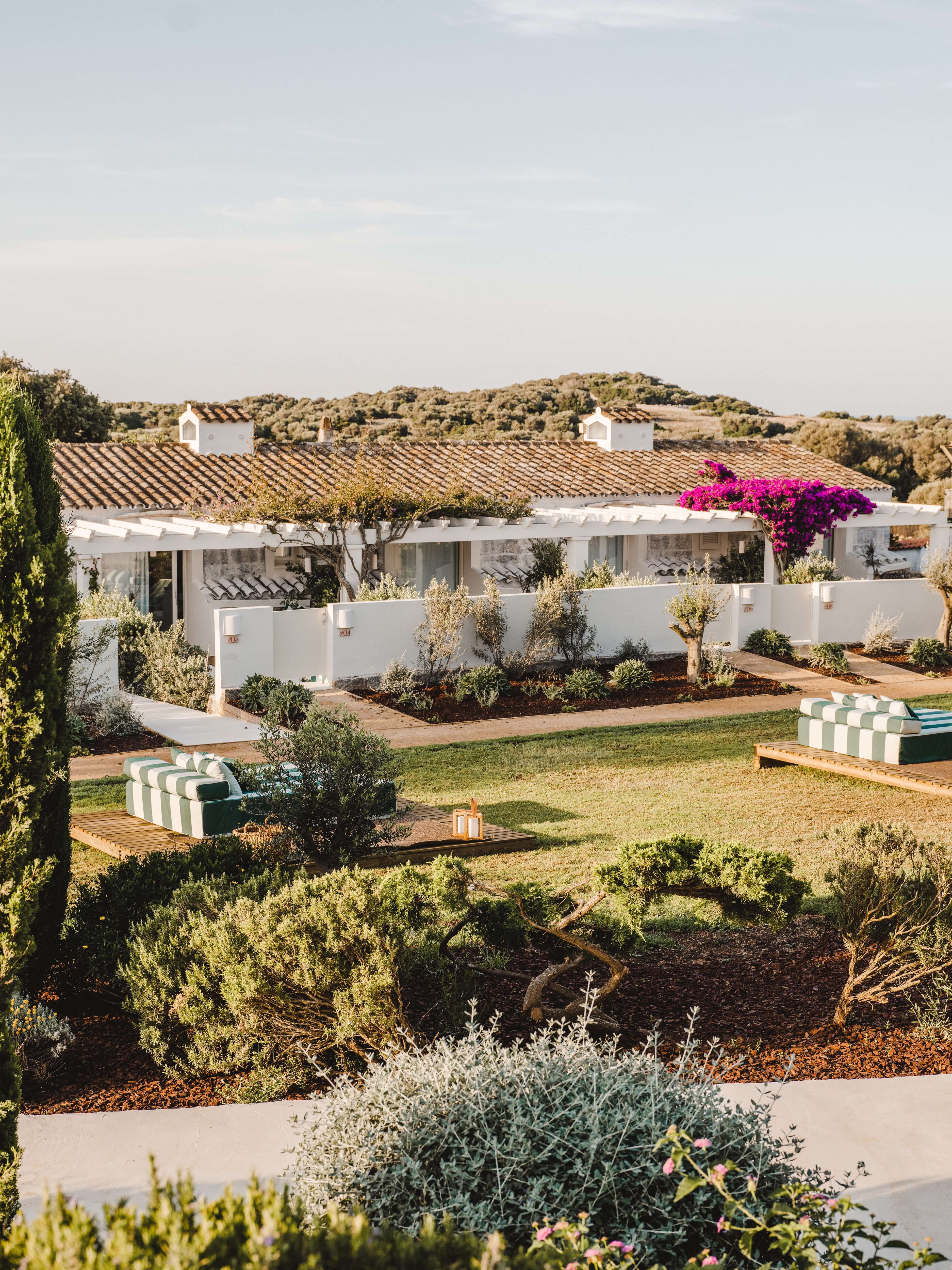 Morvedra Nou, Balearic Islands, Spain — Whitewashed Mediterranean villa with terracotta roof, vibrant bougainvillea, striped loungers, and manicured gardens under soft afternoon light.