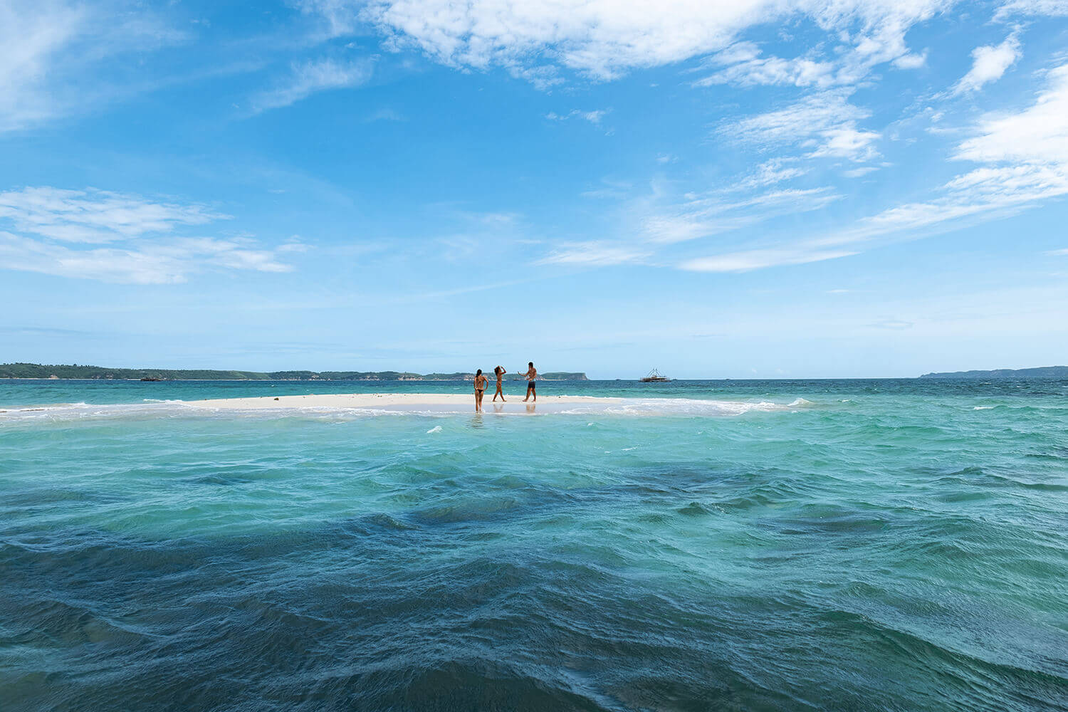 Pulau Pasir, Asia — Swimmers in turquoise water at sandy beach under blue sky, tropical coastal landscape with sailboat and forested shoreline.