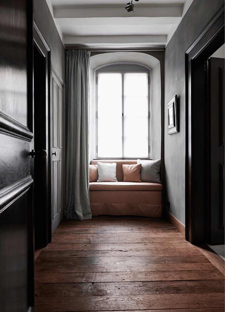 Purs, Europe — Narrow hallway with arched window, terracotta daybed, gray curtains, dark wood flooring, minimalist modern luxury interior design.