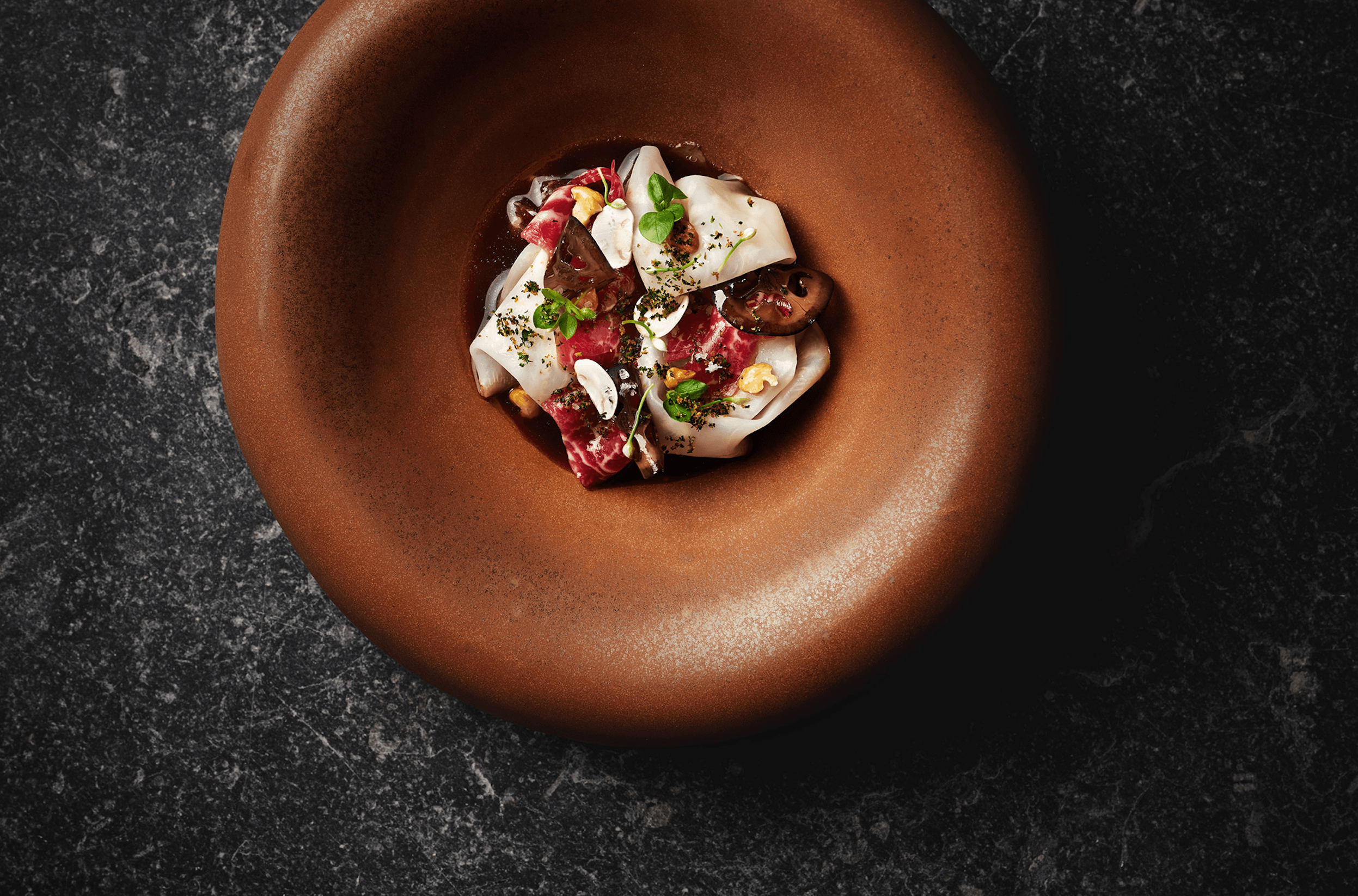 Purs, Europe — Plated charcuterie and burrata with microgreens on bronze circular dish against dark marble surface, fine dining presentation.