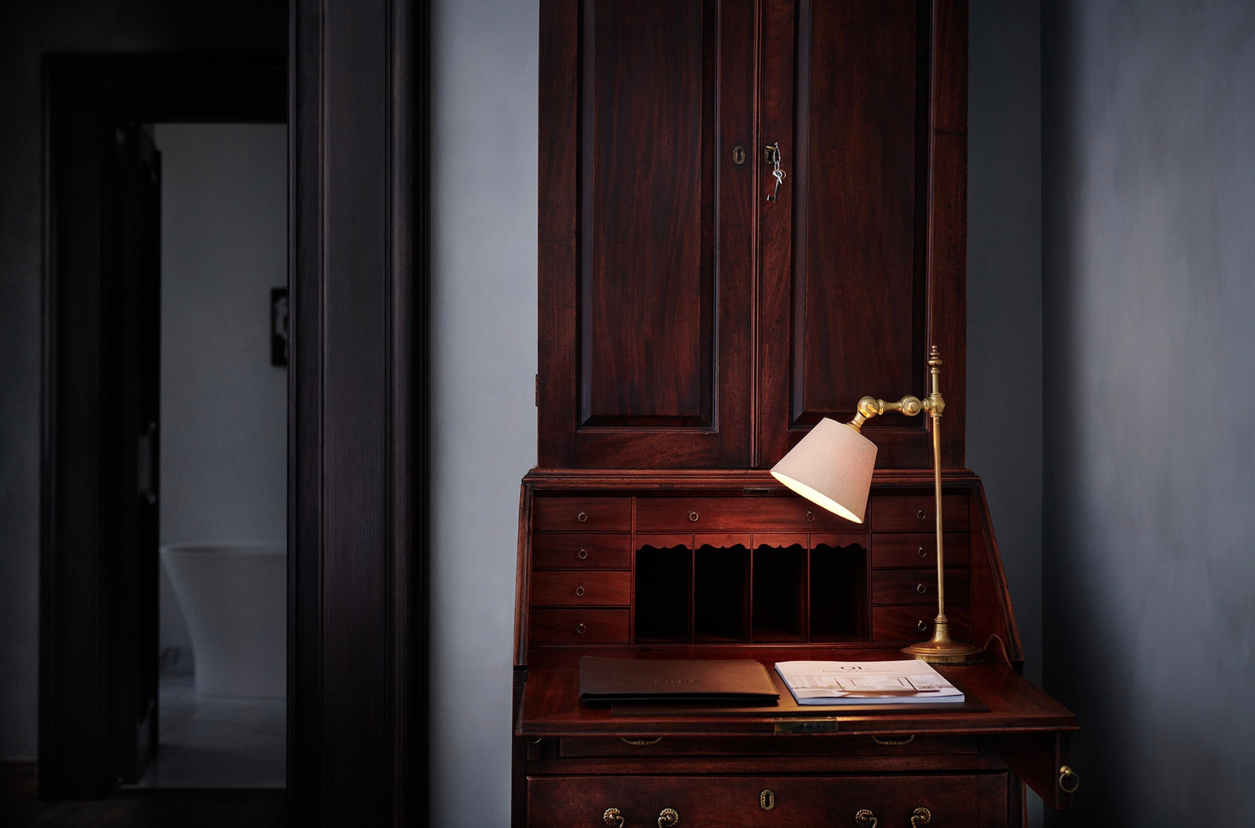 Purs, Europe — Dark wood secretary desk with brass task lamp, open notebook, and minimalist aesthetic in gallery hallway.