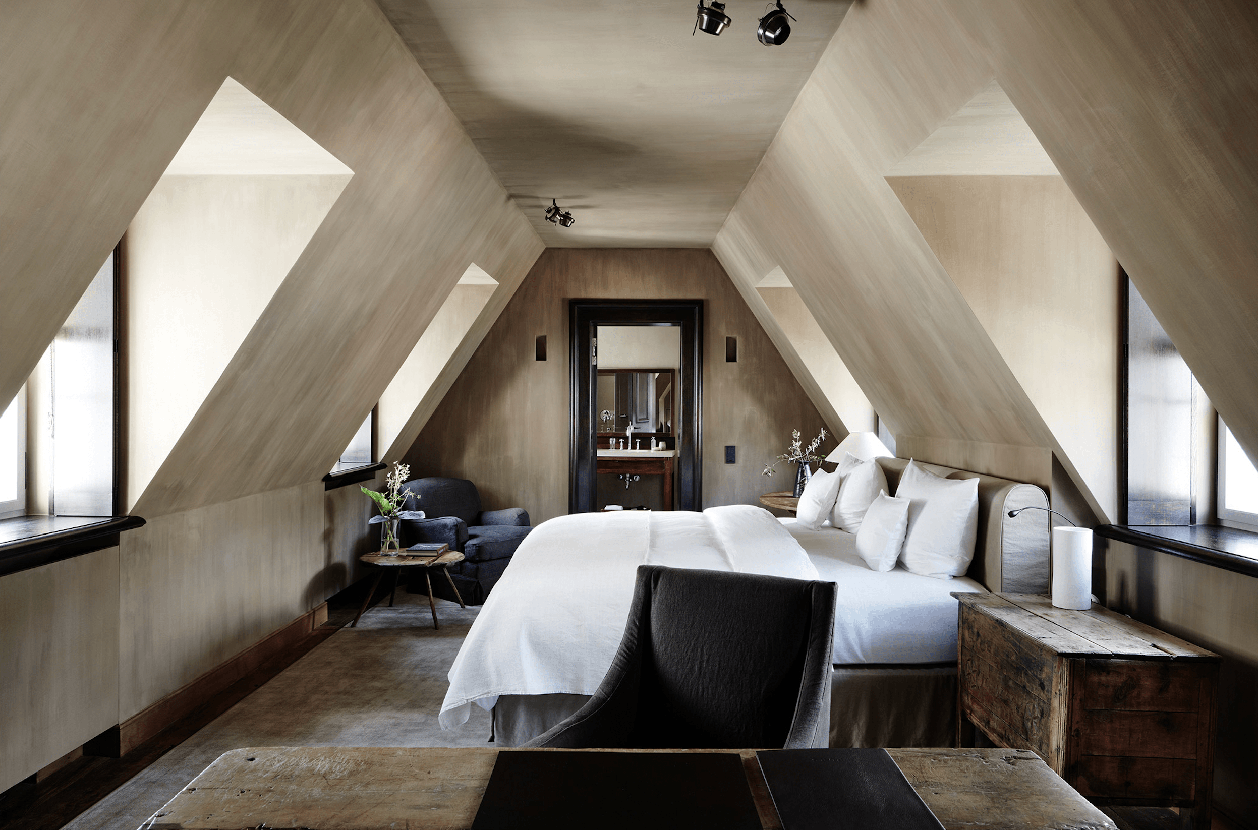 A-frame attic bedroom at Purs with bleached wood walls, skylight windows, and minimal furnishings beneath peaked ceilings.