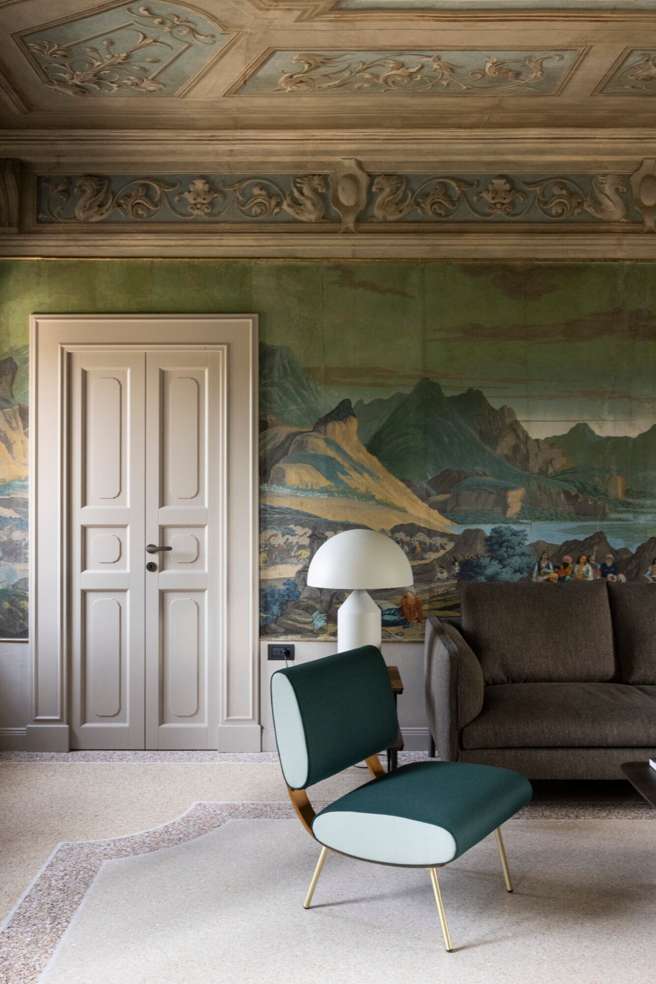 Roncolo 1888, Europe — Neoclassical room with ornate ceiling, landscape mural, modern green lounge chair, mushroom lamp, and cream paneled doors.