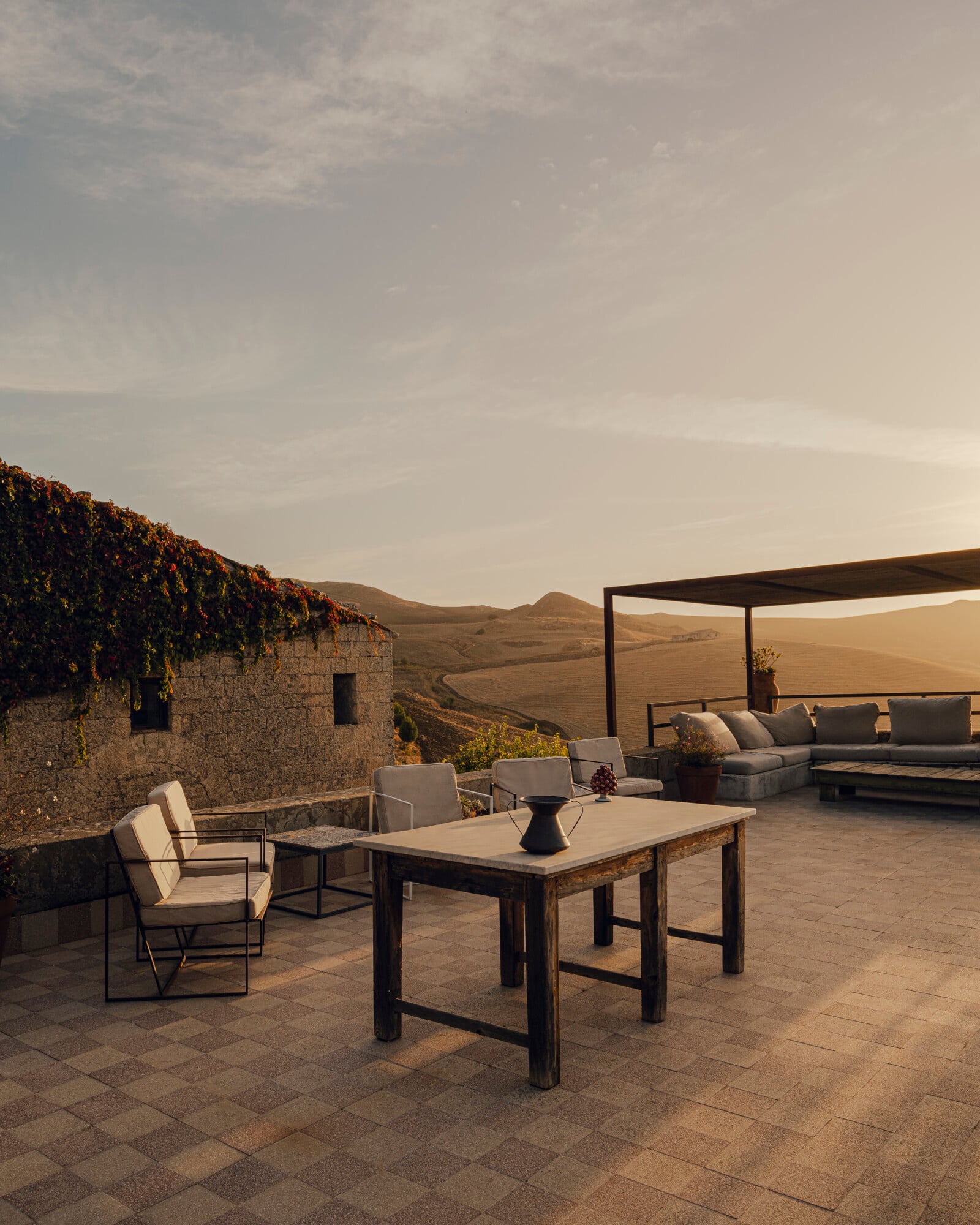 Susafa, Italy — Stone terrace with dining table, lounge seating, pergola and rolling Tuscan hills at golden hour.