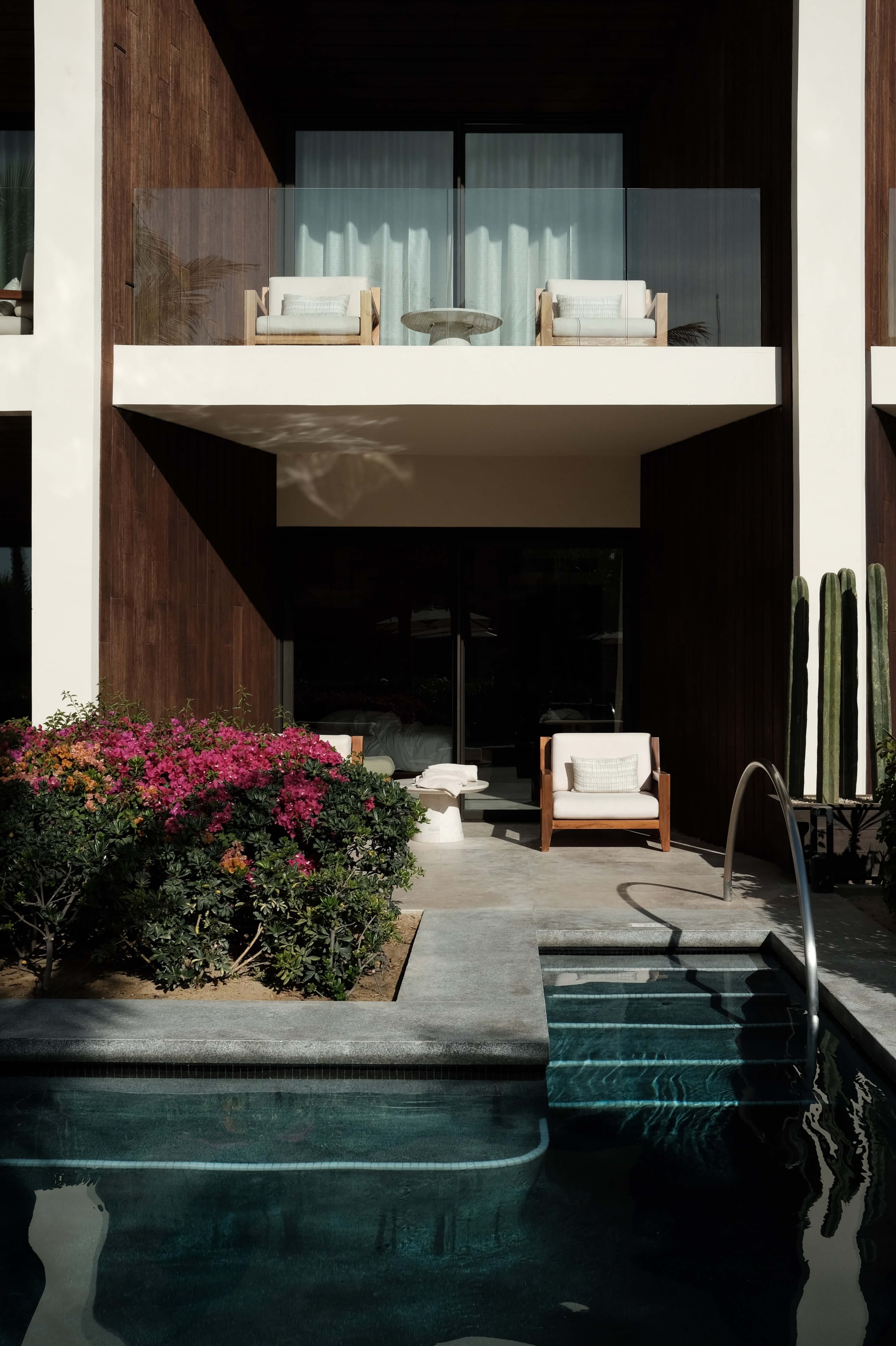 Nobu Los Cabos, Mexico — Modern concrete balcony with cream seating overlooking dark-tiled pool, magenta bougainvillea, and minimalist architecture with dark wood accents.