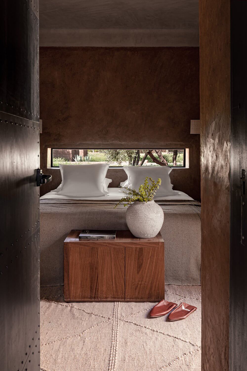 Villa D, Africa — Spa bathroom with earthen walls, white sculptural basins, wooden cabinet, natural light from horizontal window, terracotta slippers on neutral rug.