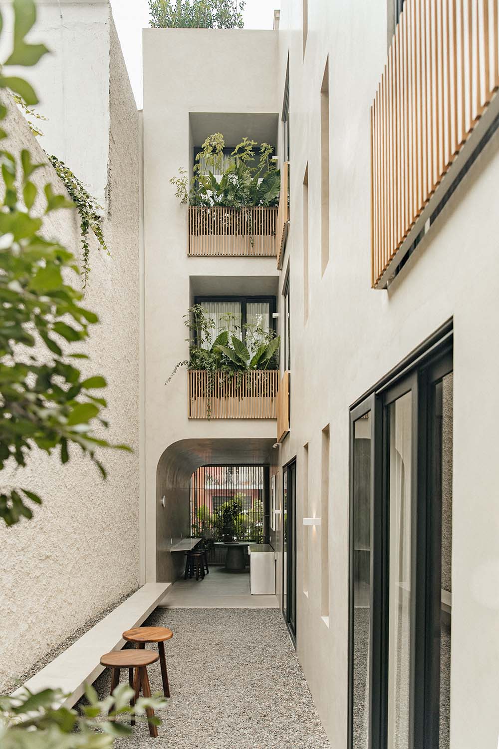 Octavia Casa, Mexico — Narrow courtyard with stacked wooden-railed balconies, white walls, potted greenery, and natural light filtering through a minimalist passage.