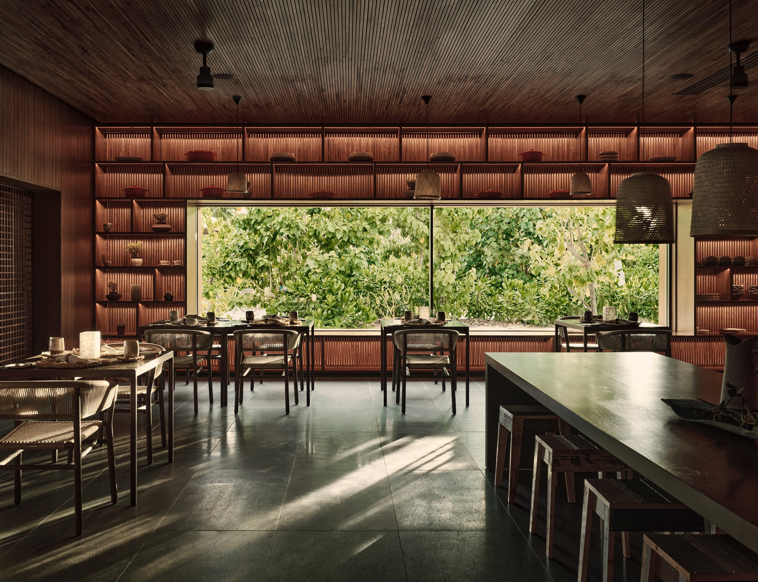 Roots, Asia — Modern timber-lined dining room with black mesh chairs, polished concrete floors, and floor-to-ceiling windows framing lush green landscape.