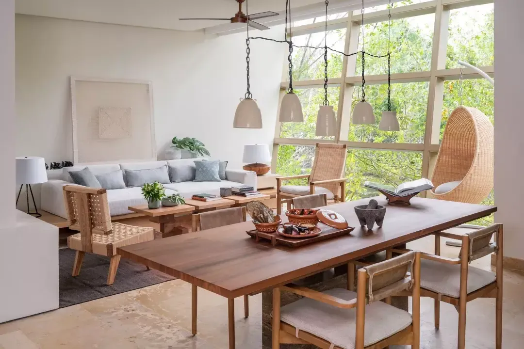 Rosewood Mayakoba, Mexico — Modern dining room with warm wood table, woven pendant lights, floor-to-ceiling windows overlooking tropical foliage, and mid-century lounge seating.