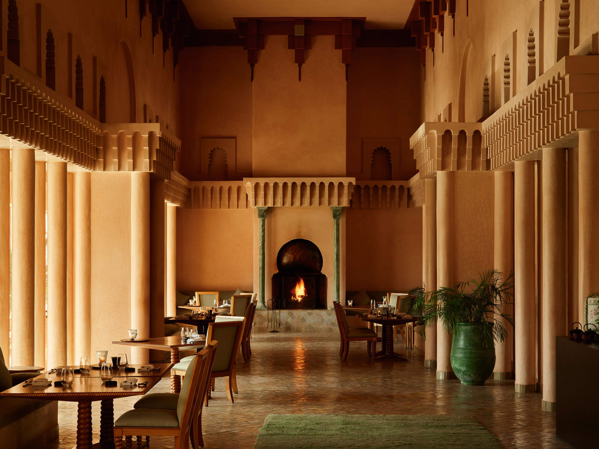 Amanjena, Marrakech, Morocco — Ochre courtyard with colonnade, arched fireplace, candlelit dining tables, and green ceramic vessels in minimalist Moroccan design.