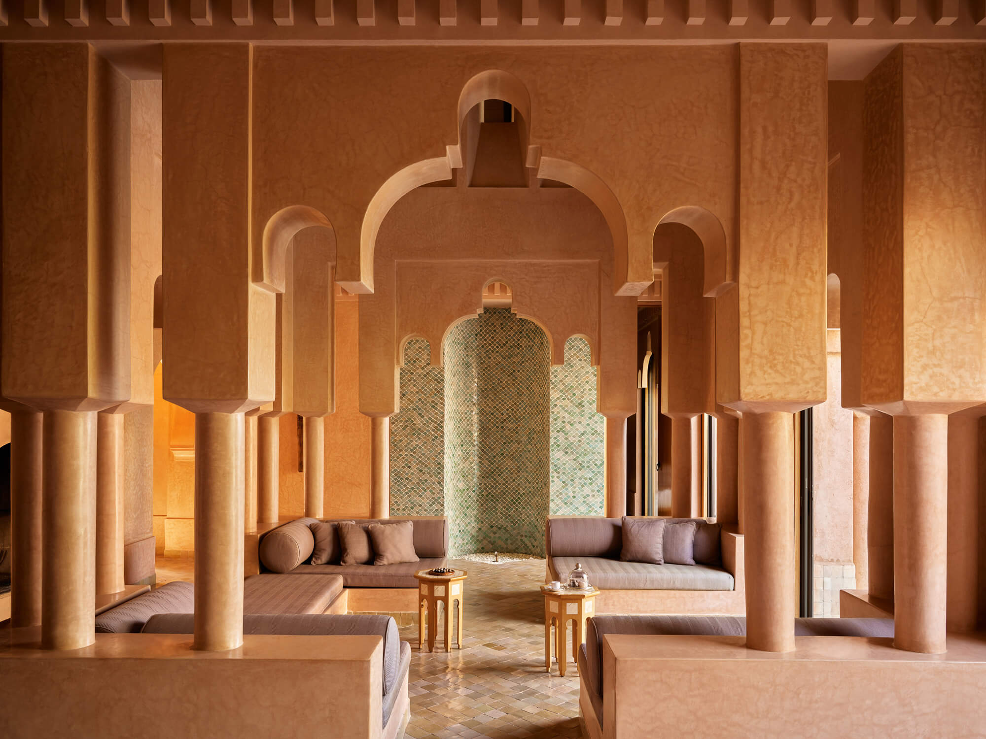 Amanjena, Africa — Ochre-walled courtyard with arched colonnades, zellige-tiled fountain, and taupe seating beneath warm natural light.