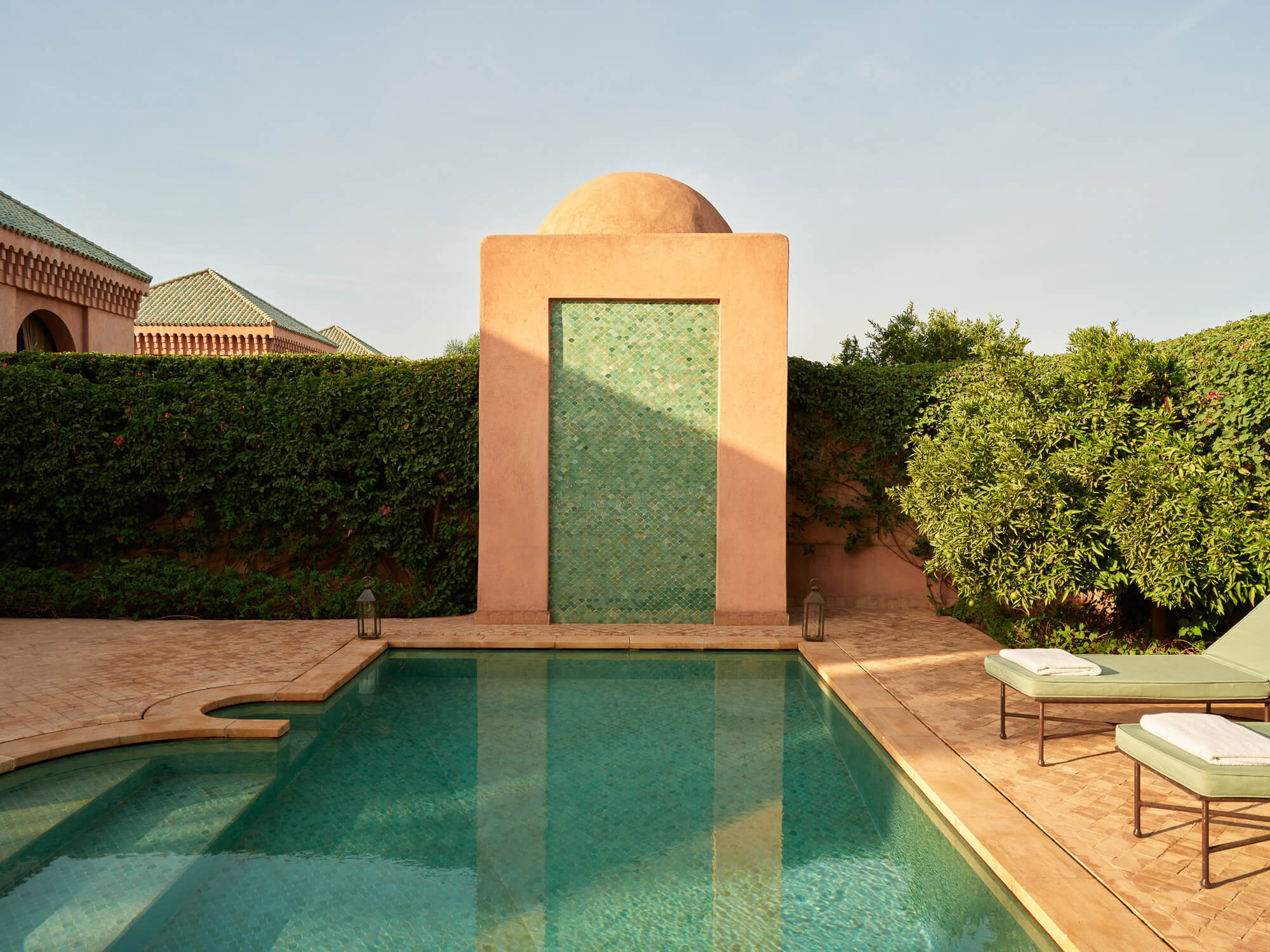 Amanjena, Morocco — Turquoise pool with geometric tile feature wall and dome, terracotta courtyard surrounded by manicured hedges, minimalist Moroccan architecture.