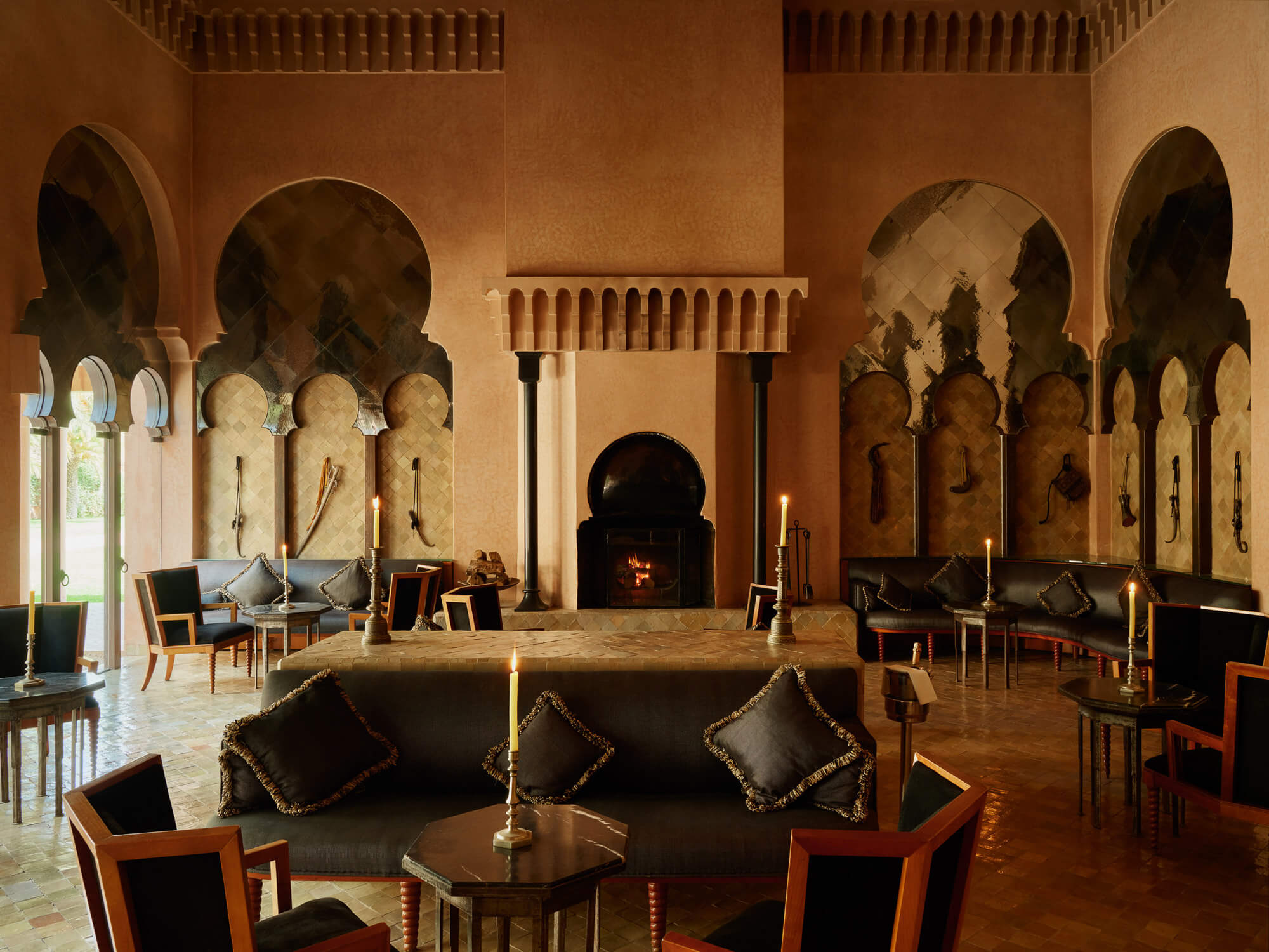 The Bar, Africa — Moroccan-inspired lounge with arched doorways, terracotta walls, black leather seating, brass candlesticks, and glowing fireplace.