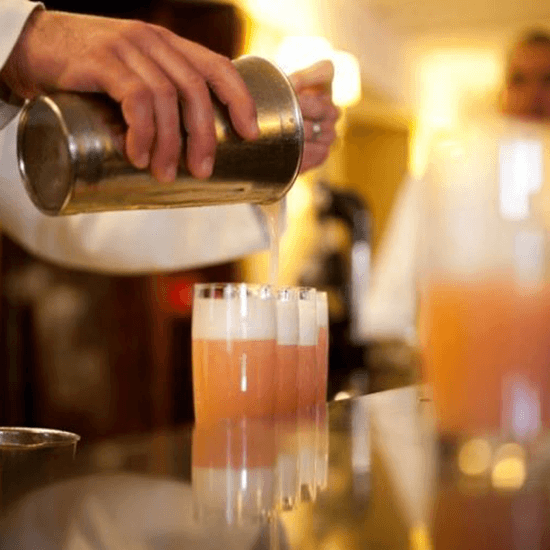  Harry’s Bar at Cipriani — Bartender pouring amber cocktail from brass mixing vessel into crystal glass, warm ambient lighting, luxury hospitality setting.