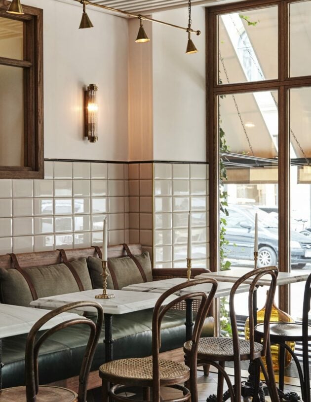 Sanders Kitchen, Europe — Banquette seating with striped cushions, bentwood chairs, marble-top tables, pendant lights, and gridded windows overlooking street.