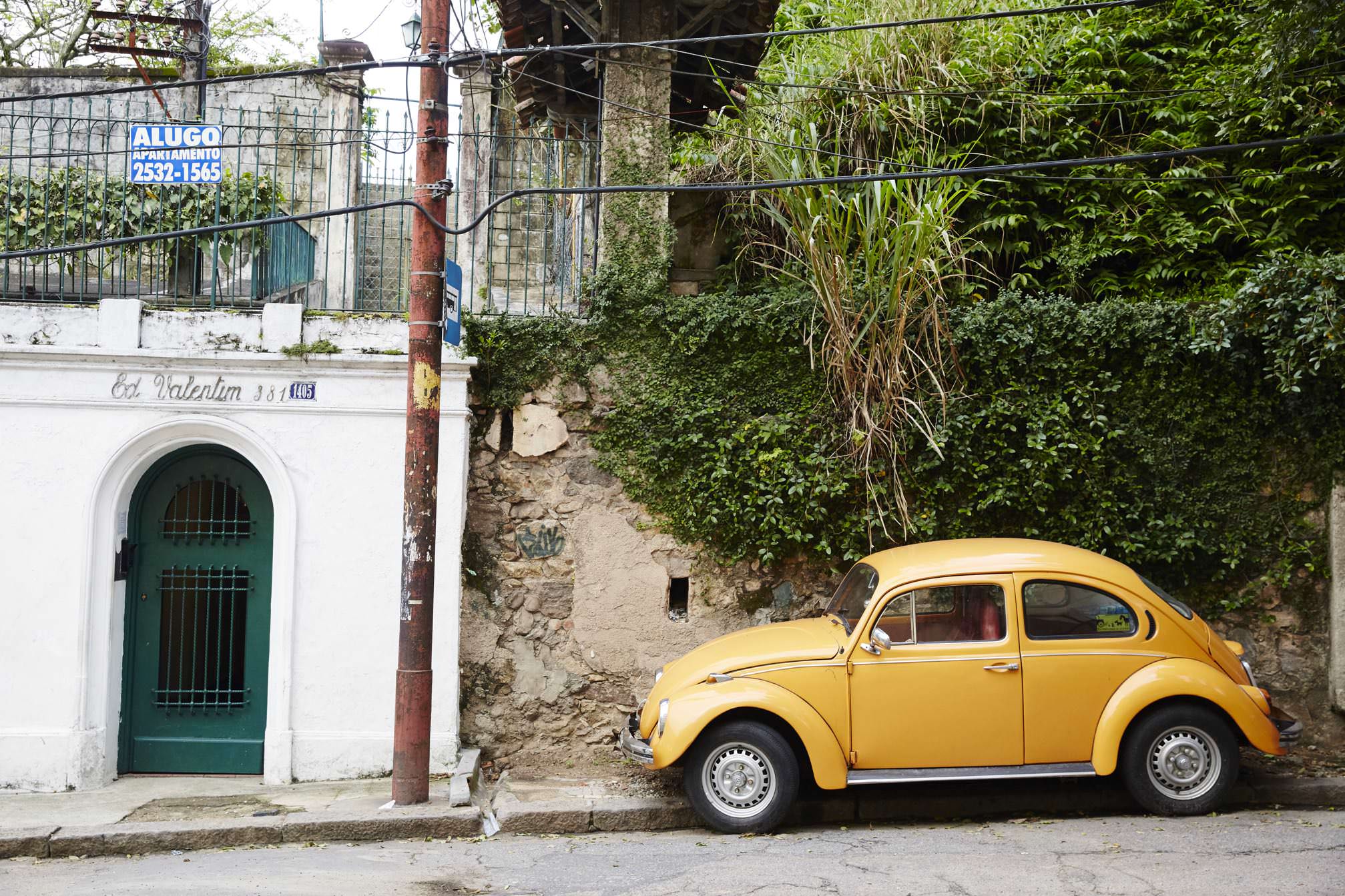 Yellow Volkswagen Beetle parked on weathered street in Santa Teresa with colonial architecture, ivy-covered walls, and green arched doorway.