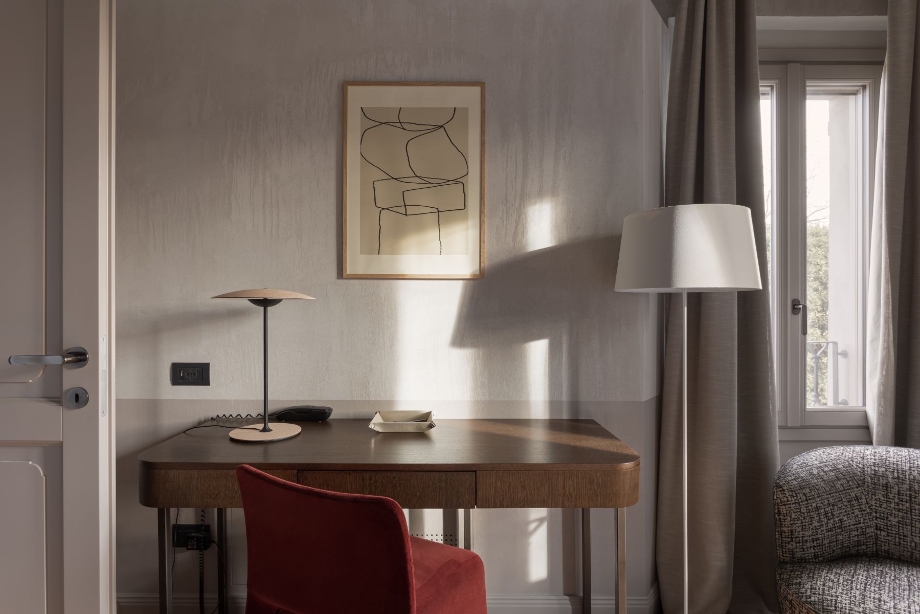 Roncolo 1888, Europe — Minimalist hotel desk with walnut wood, burgundy chair, warm natural light, line-art wall print, modern task lighting.