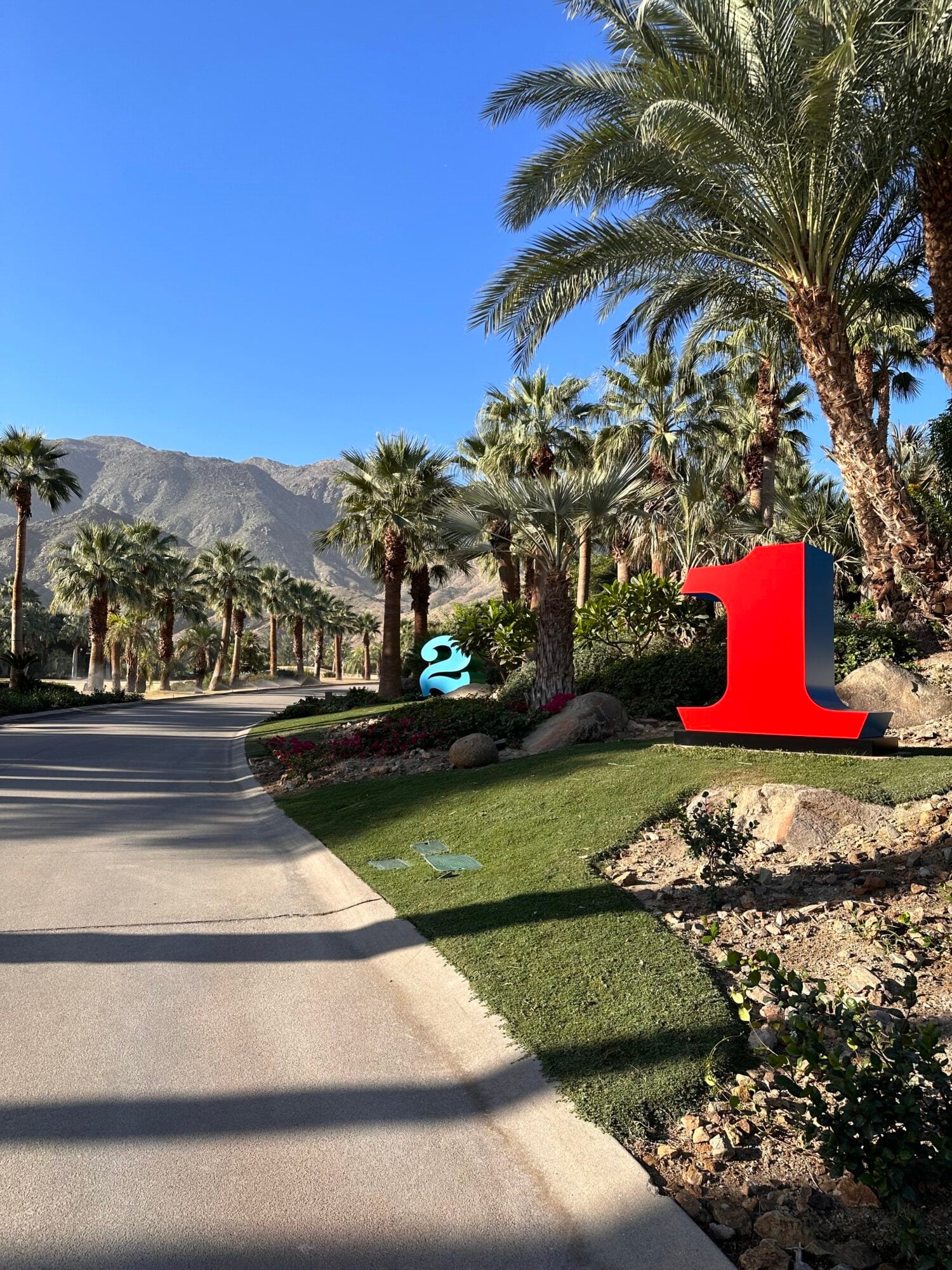Sensei Porcupine Creek, North America — Palm-lined driveway with sculptural red signage, manicured grounds, and desert mountain backdrop under clear sky.