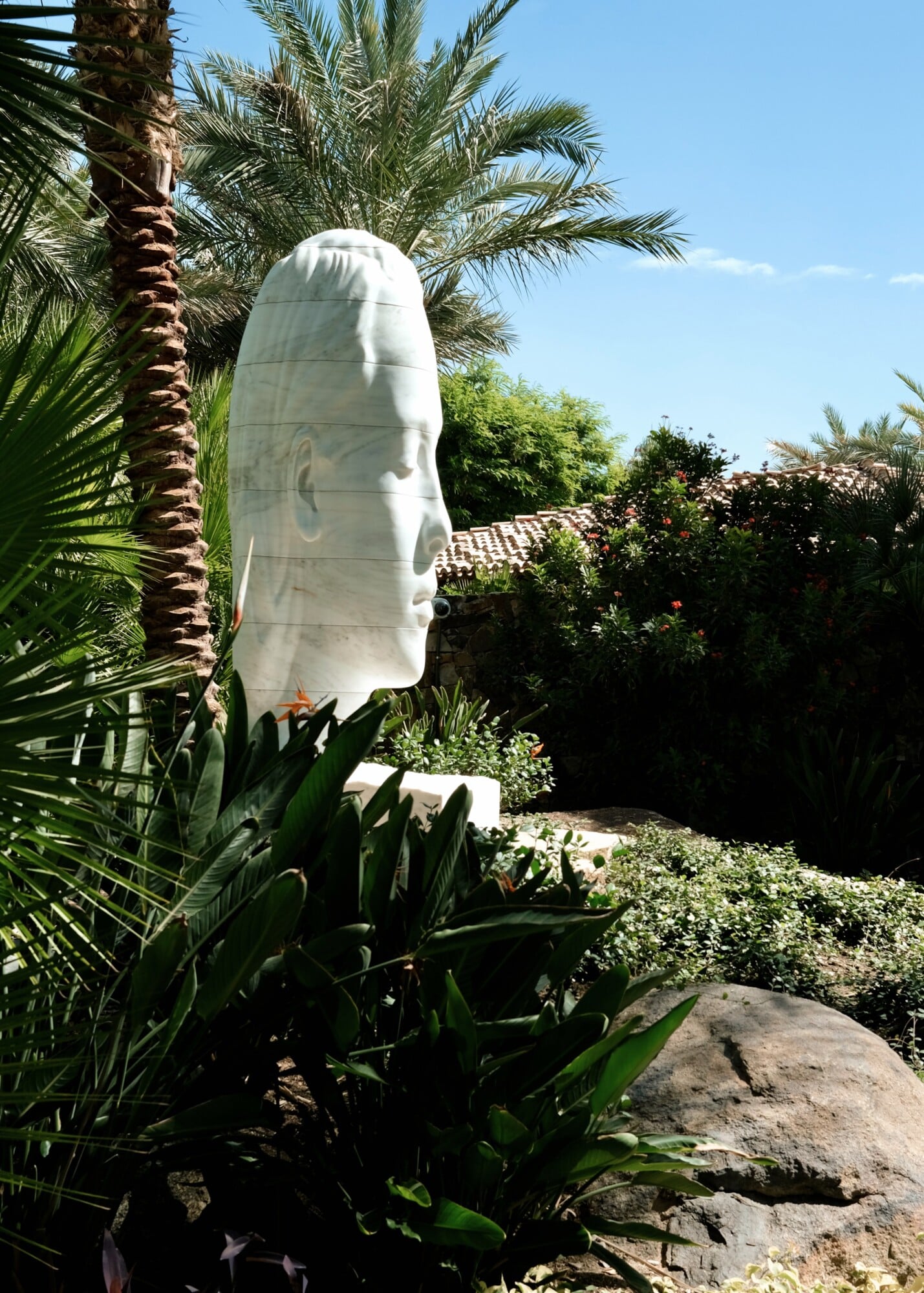 Sensei Porcupine Creek, North America — White marble head sculpture among palm trees and flowering vines in Mediterranean garden courtyard.