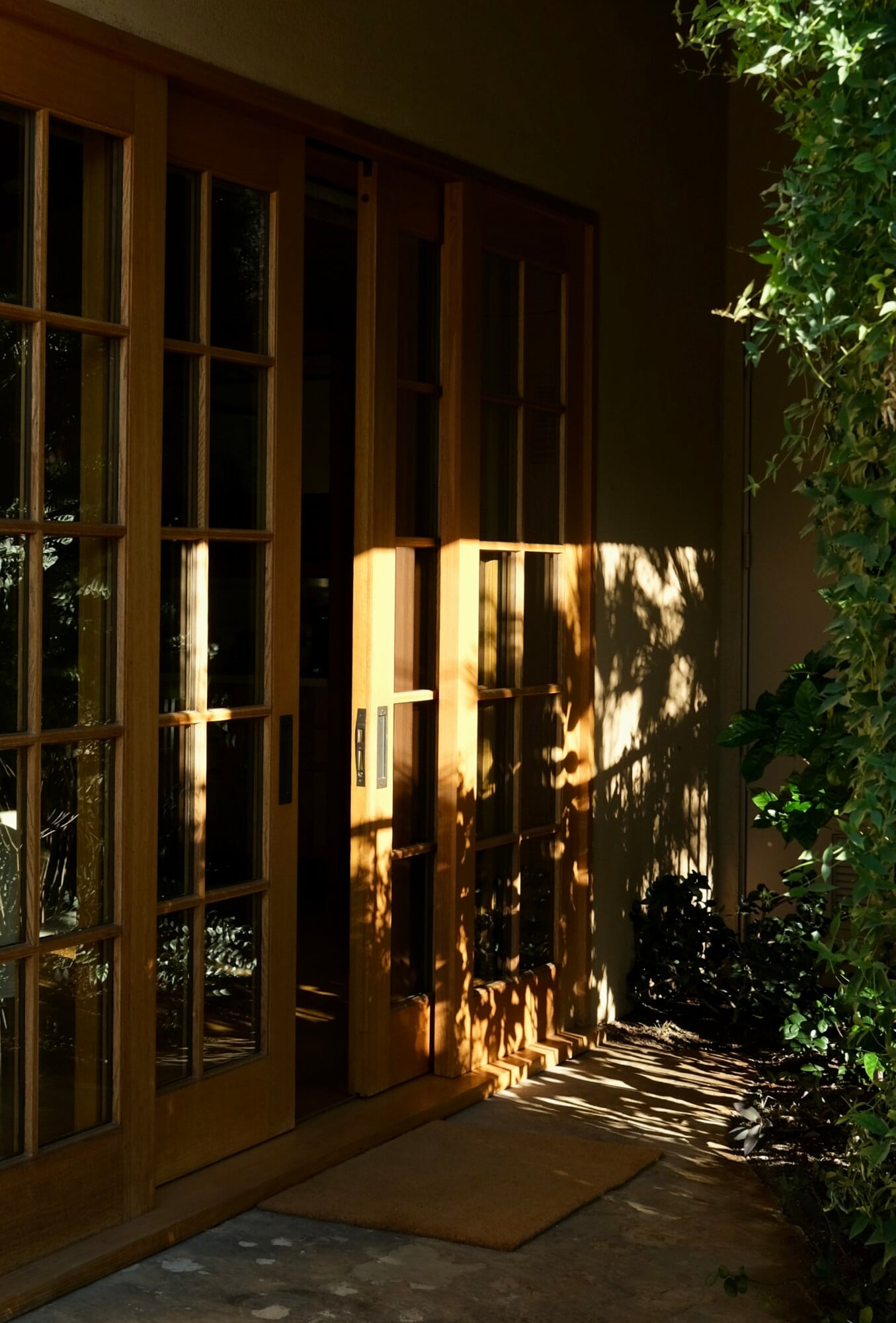 Sensei Porcupine Creek, North America — Wooden-framed glass doors casting geometric shadows on stone courtyard at golden hour, surrounded by climbing ivy.