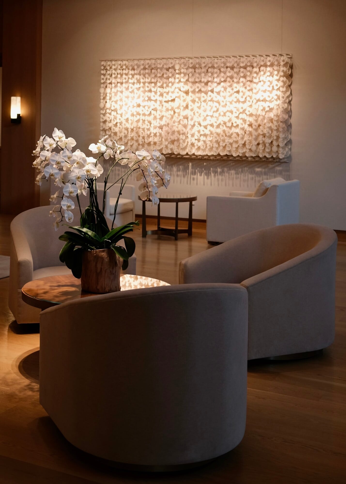 Sensei Porcupine Creek, North America — Minimalist lounge with curved cream chairs, white orchids, and illuminated sequin wall art creating warm ambient luxury interior.
