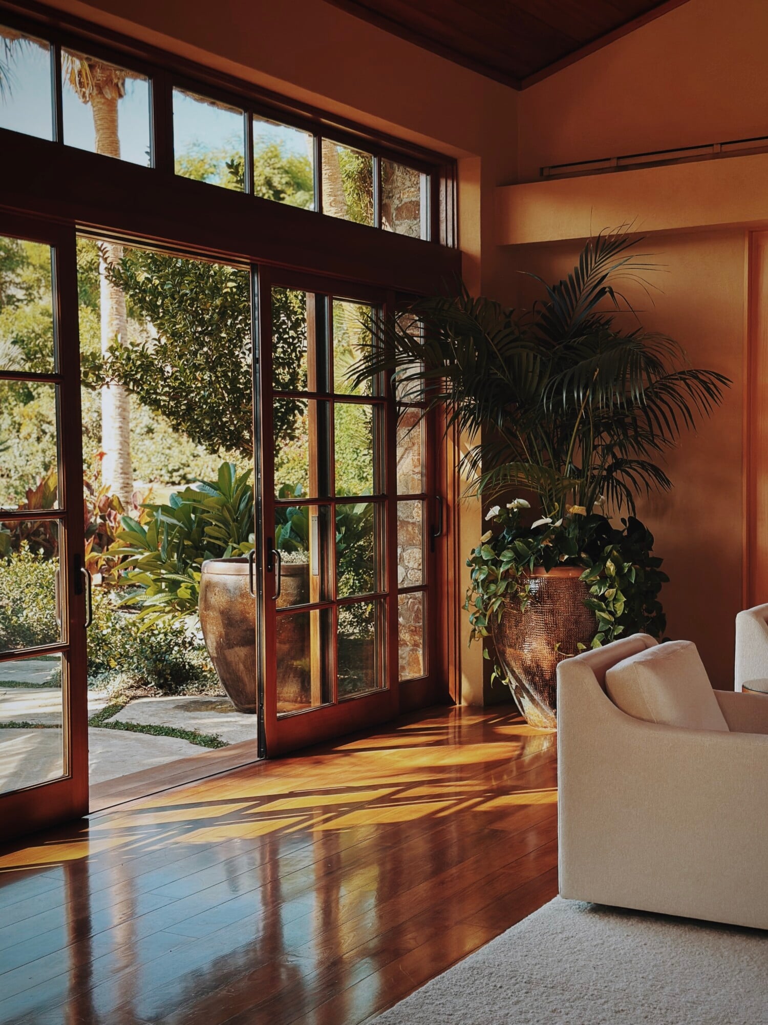 Sensei Porcupine Creek, North America — Terracotta-walled living room with dark wood-frame glass doors, polished concrete flooring, potted palms, and cream furniture overlooking garden courtyard.