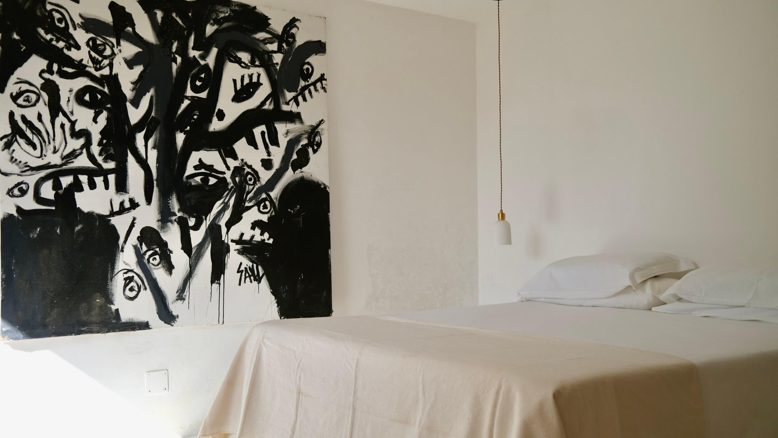 Parco Dei Sesi, Europe — minimalist bedroom with white bedding, bold black abstract artwork, pendant brass light fixture, and clean modernist interior design.